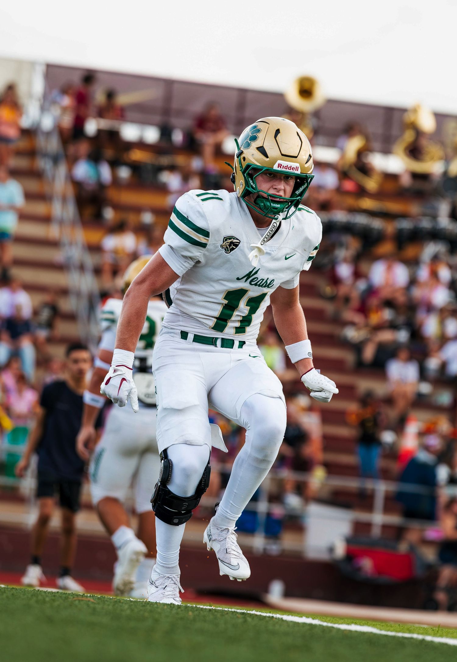 Football player #11 in green and white Mesa uniform celebrates on field during a high school game.