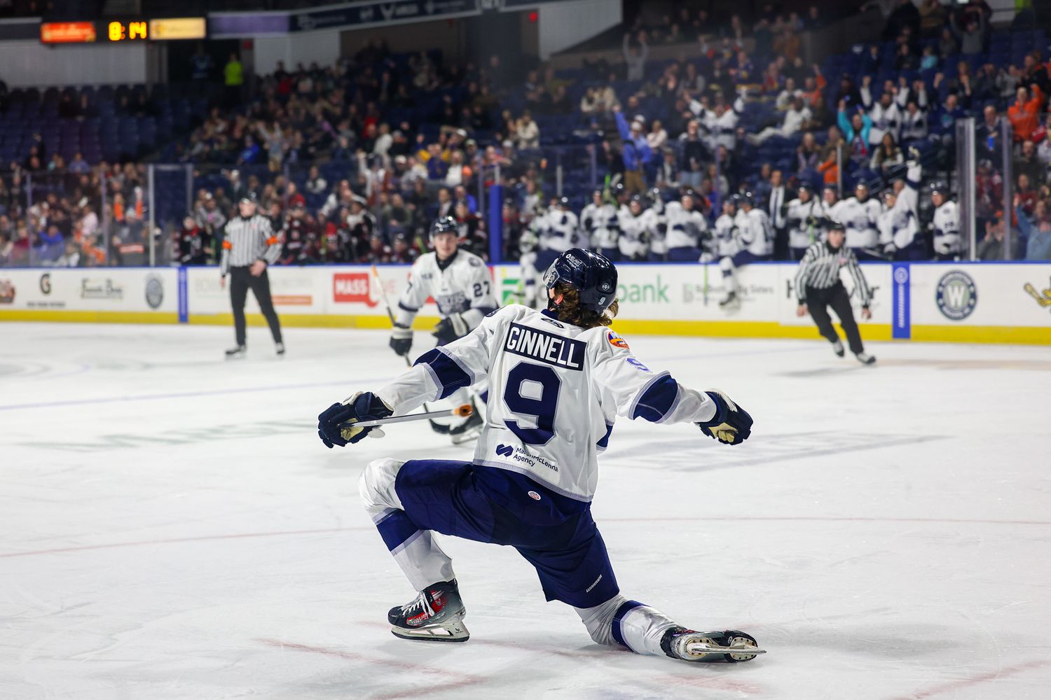 Hockey player #9 Connell celebrates on ice knees sliding after scoring a goal in a packed indoor arena.