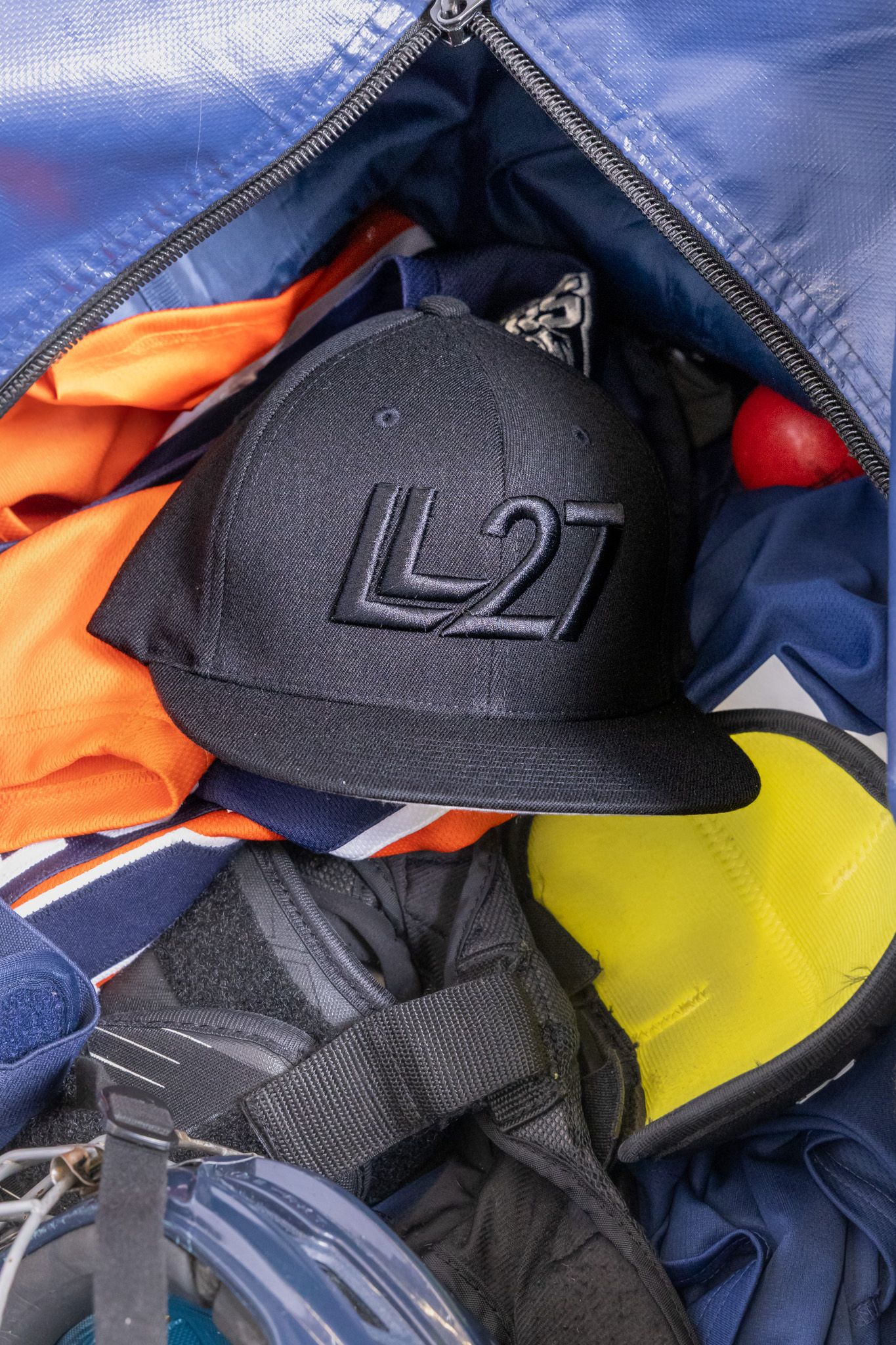 Black snapback cap with L27 logo resting inside an open sports bag with colorful gear.