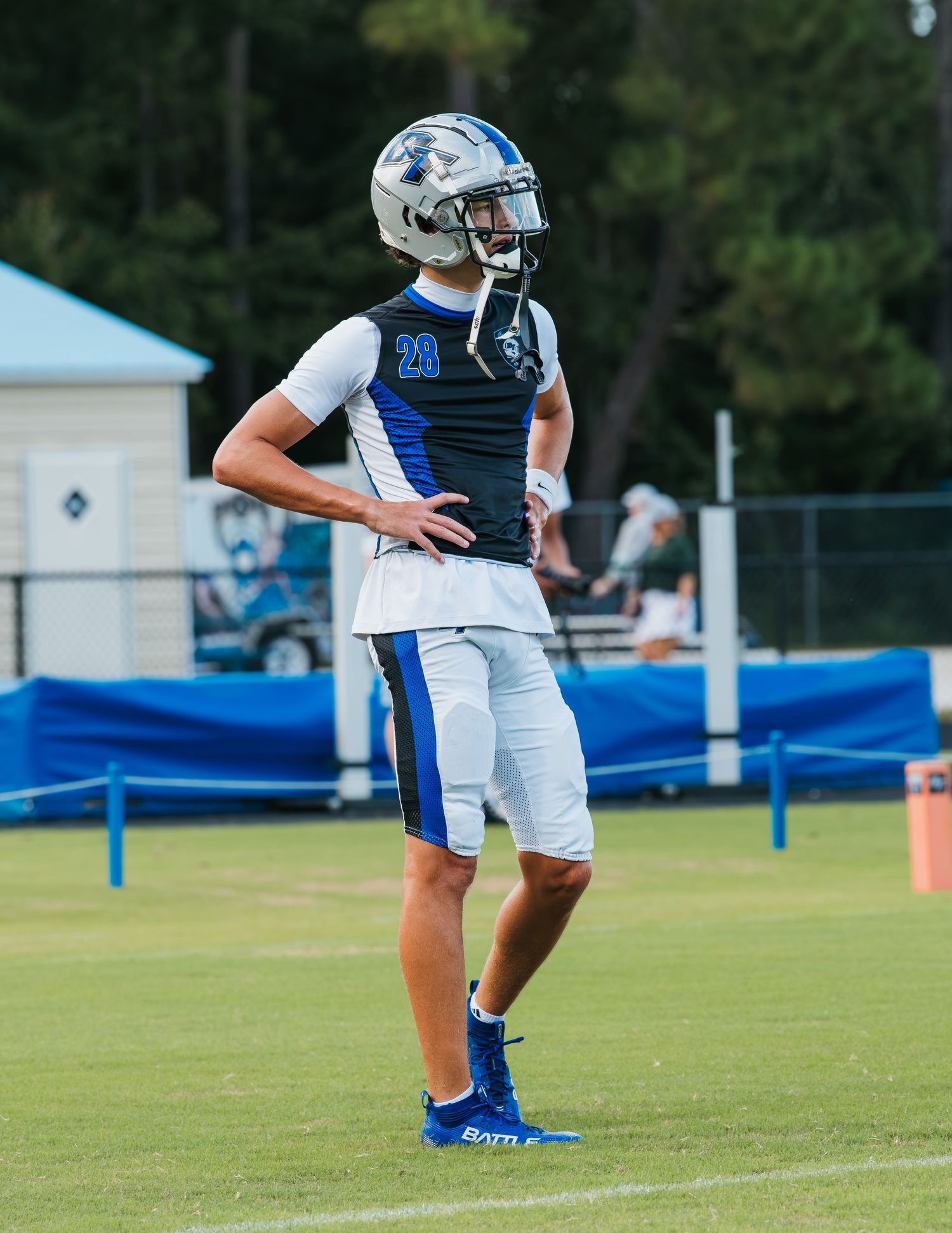 Football player wearing number 20 in blue and white uniform with helmet stands on green field during practice.