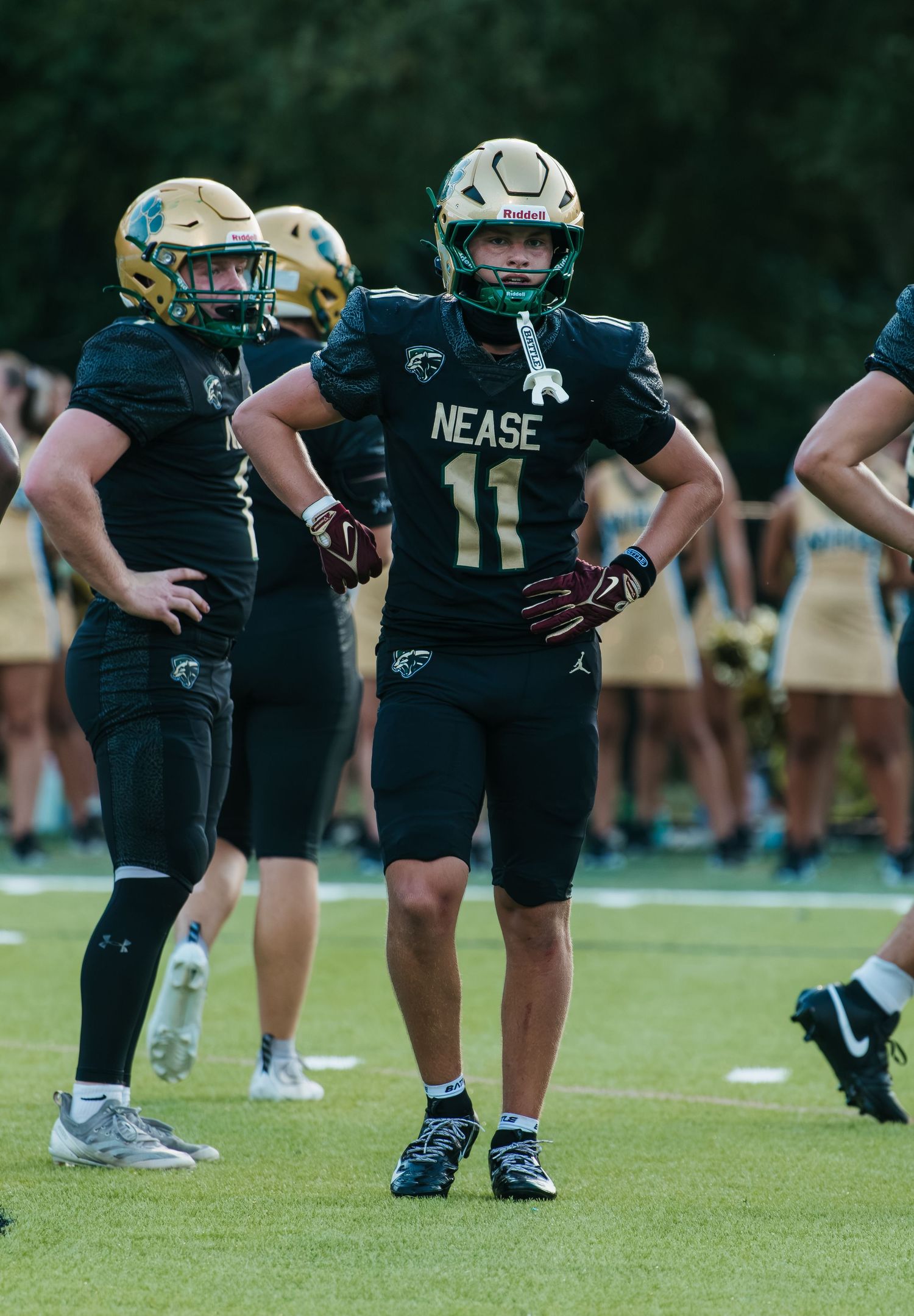 Nease High School football player #11 in black uniform stands on field during game.