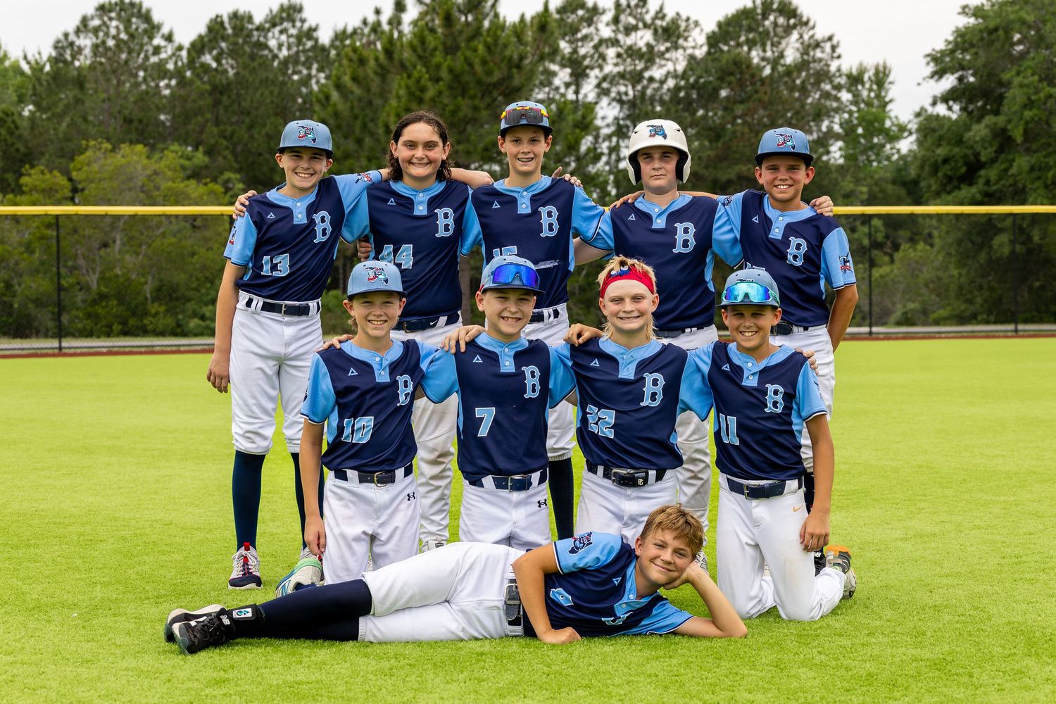 Youth baseball team in blue uniforms posing together on a green field for a group photo.