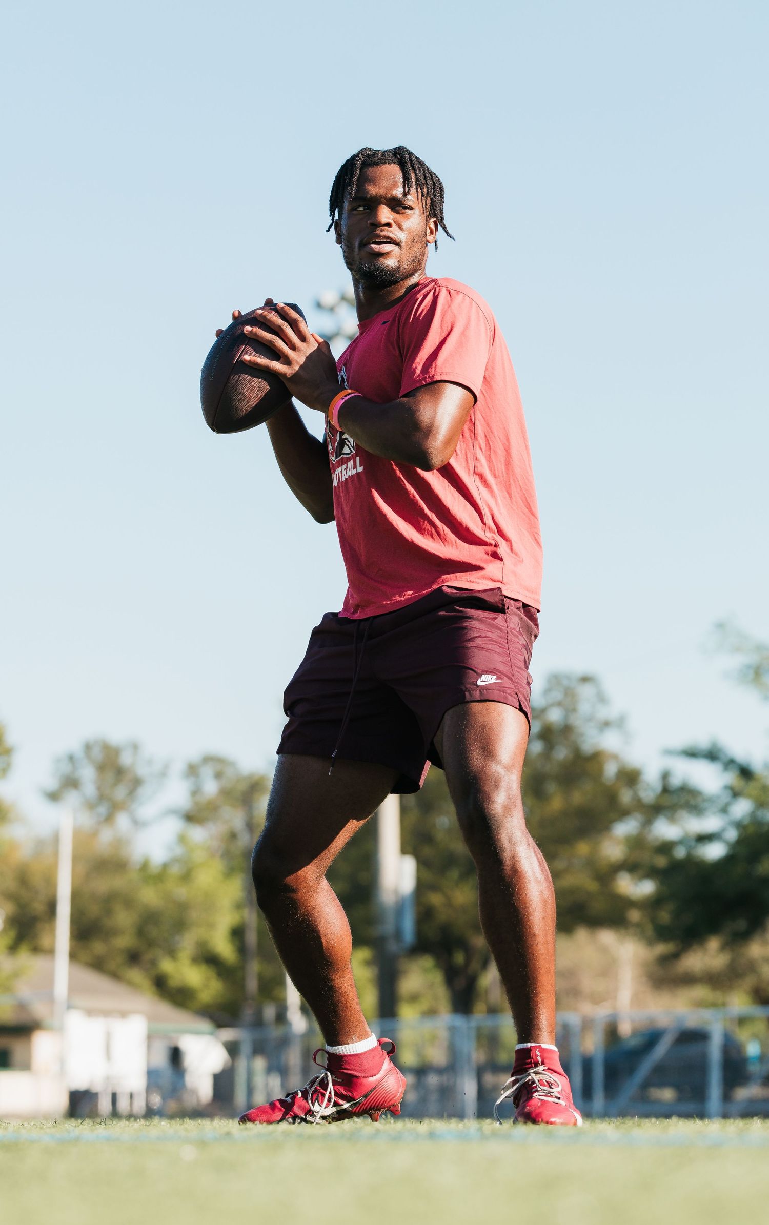 Young male athlete in red shirt poised to throw a football on a green field outdoors.