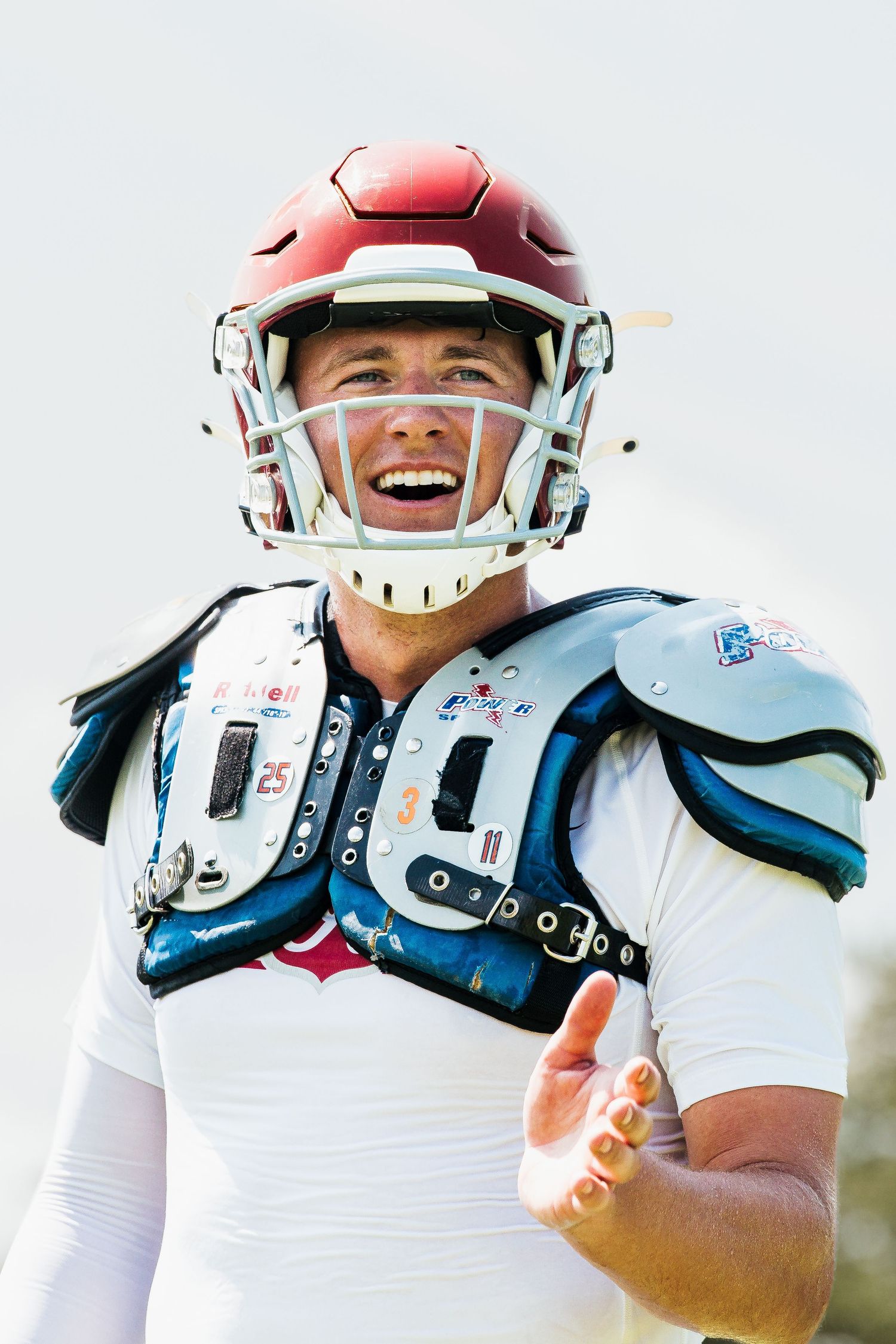 Smiling American football player in red helmet and shoulder pads wearing white uniform during outdoor game.