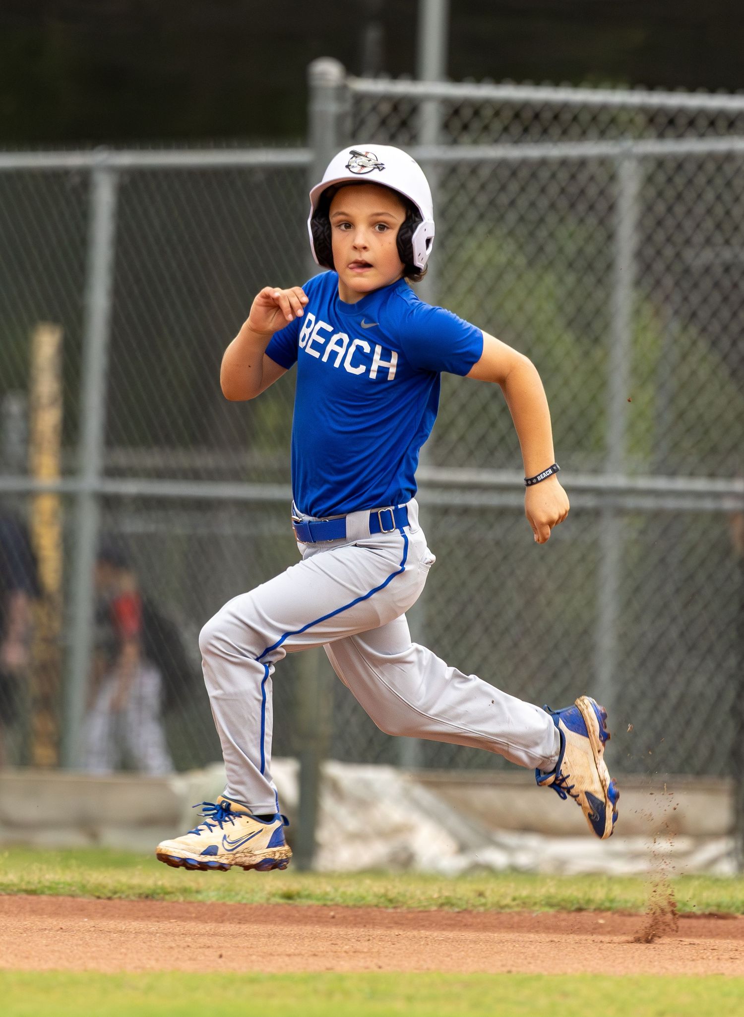 Young baseball player in blue Beach jersey and helmet sprinting bases during a little league game.
