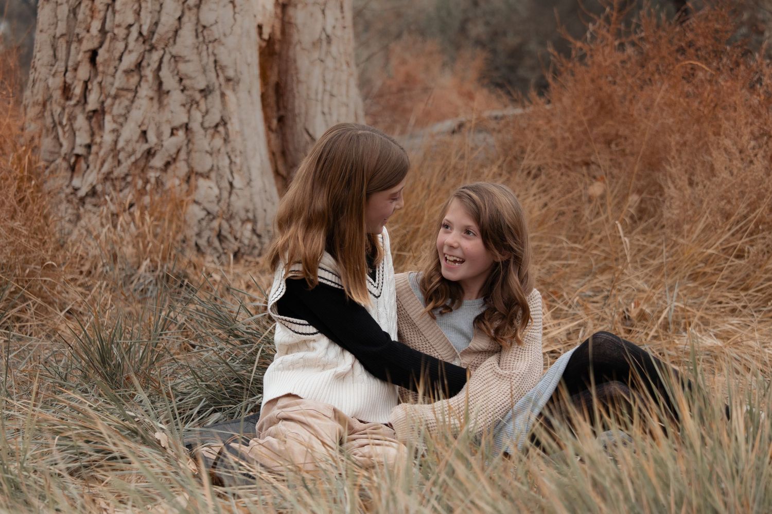 Two sisters sharing a sweet moment while sitting in tall autumn grass during outdoor family session in Richland WA