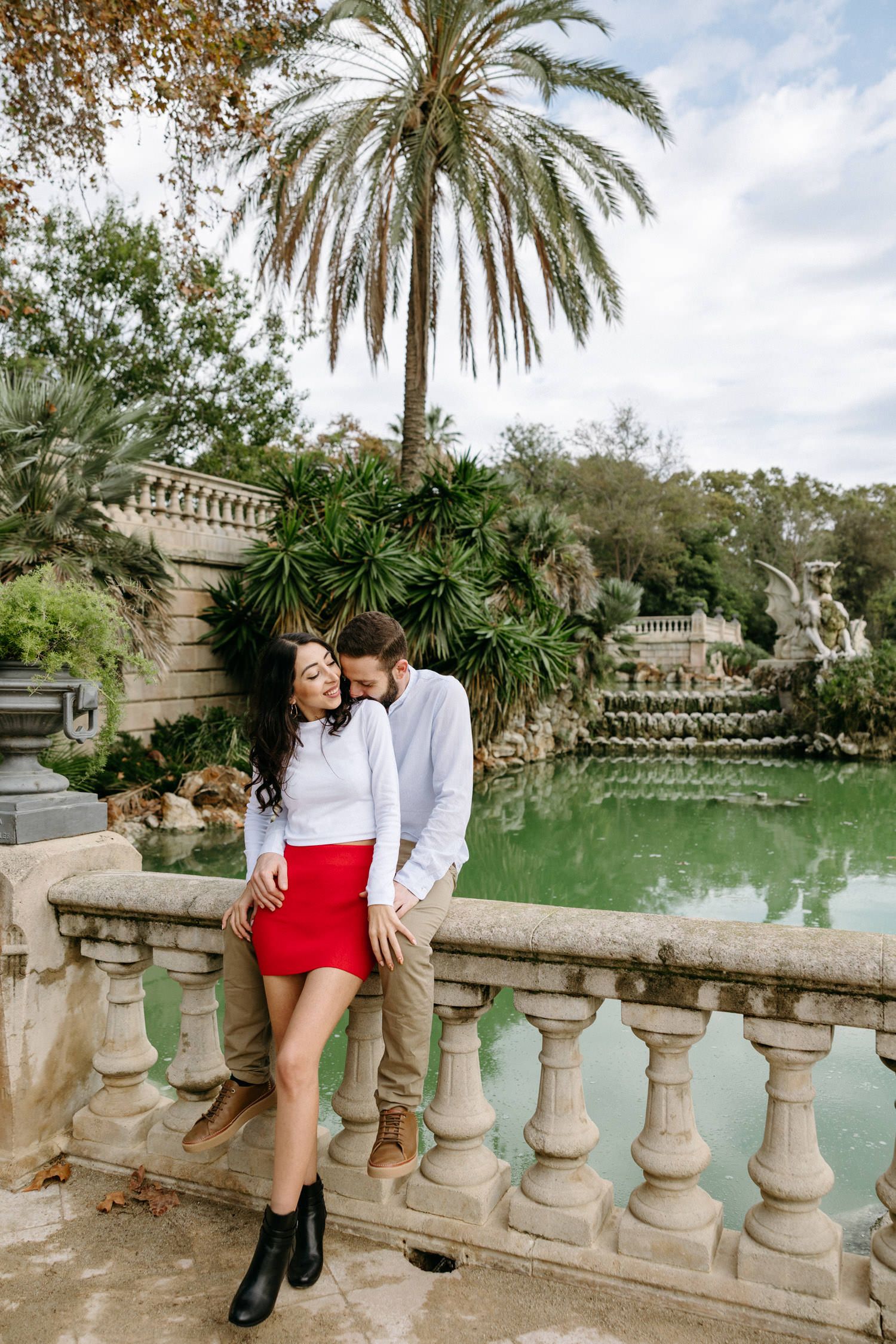 Couple poses along ornate balustrade overlooking serene pond with palm trees.