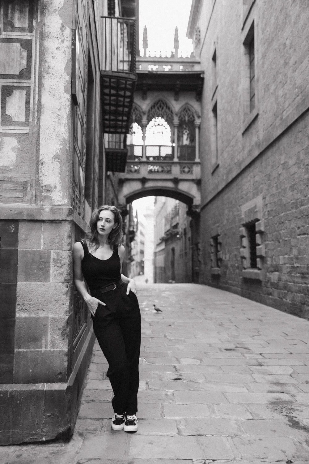 Black and white photograph of a Gothic archway bridge connecting buildings in Barcelona's historic Gothic Quarter.
