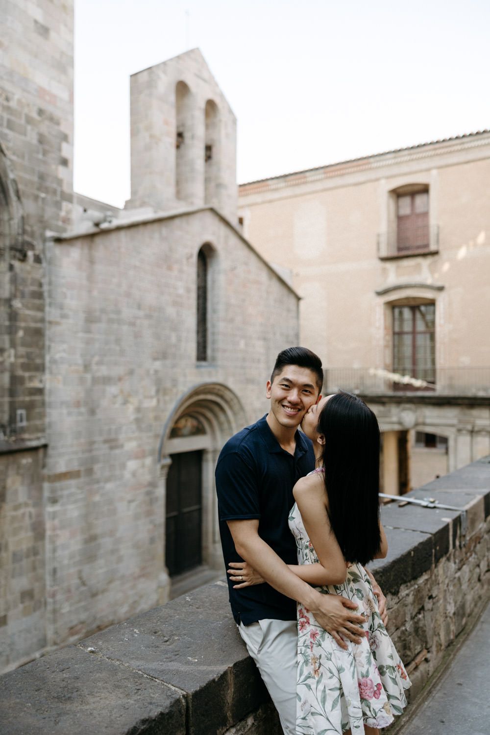A romantic couple embraces against historic stone architecture in Barcelona's Gothic Quarter.