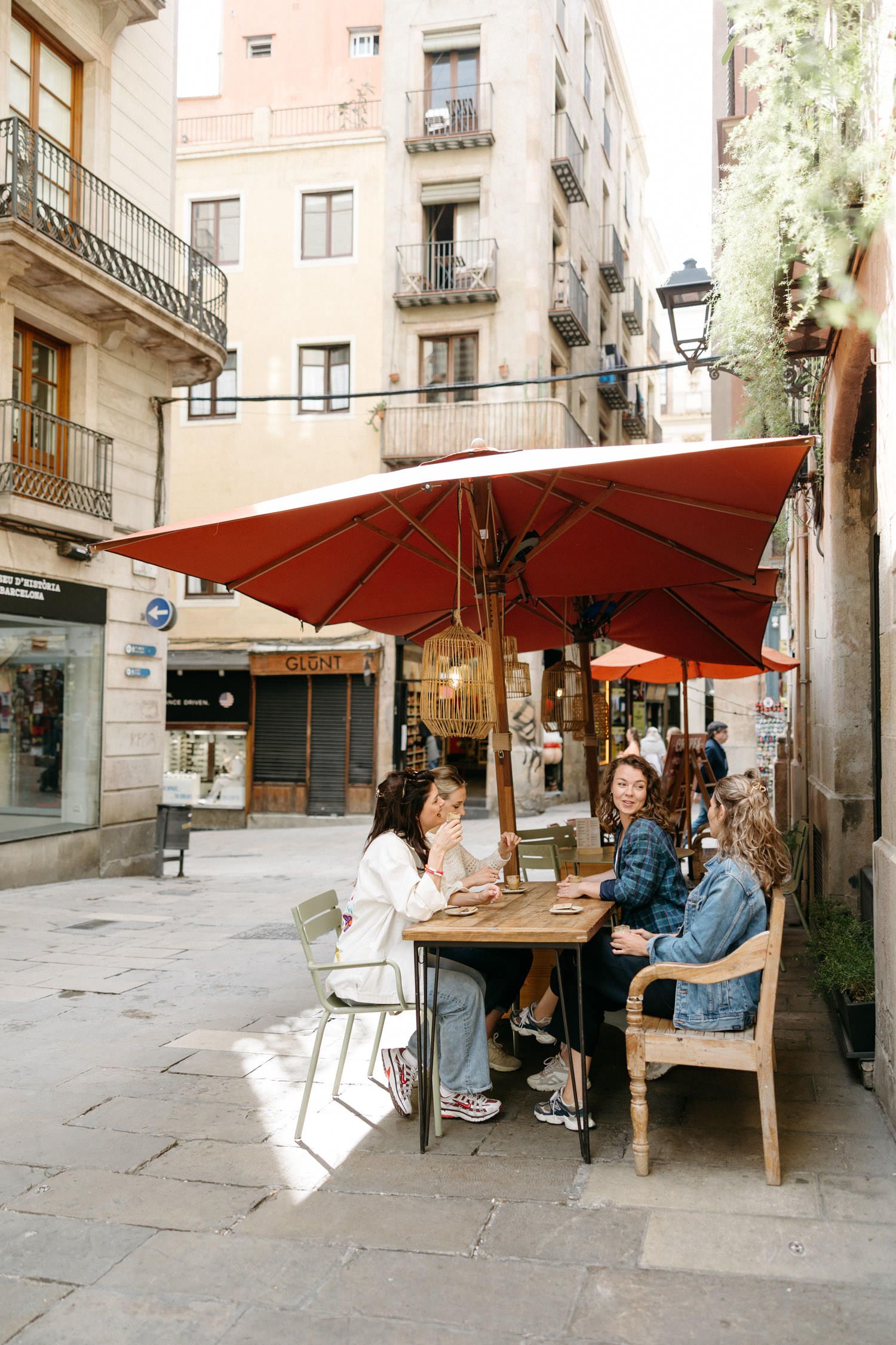 People relaxing at outdoor cafe tables under red umbrellas in a charming Barcelona plaza.