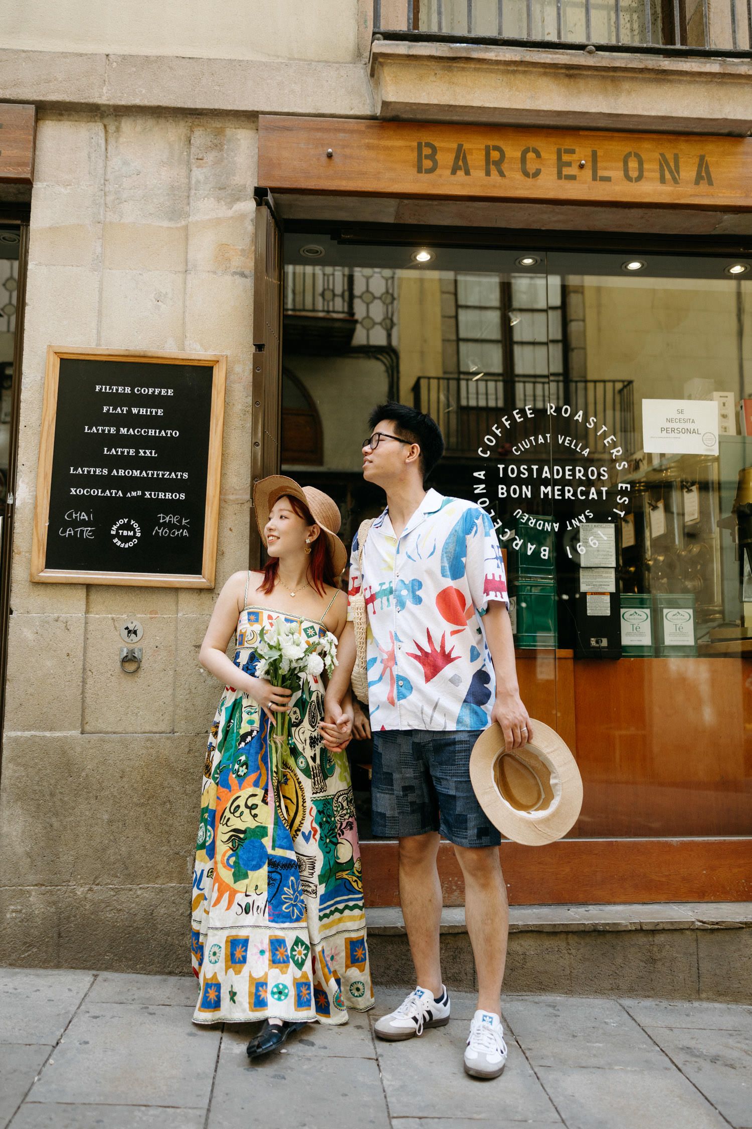 Couple in colorful matching outfits poses playfully against Barcelona street walls.