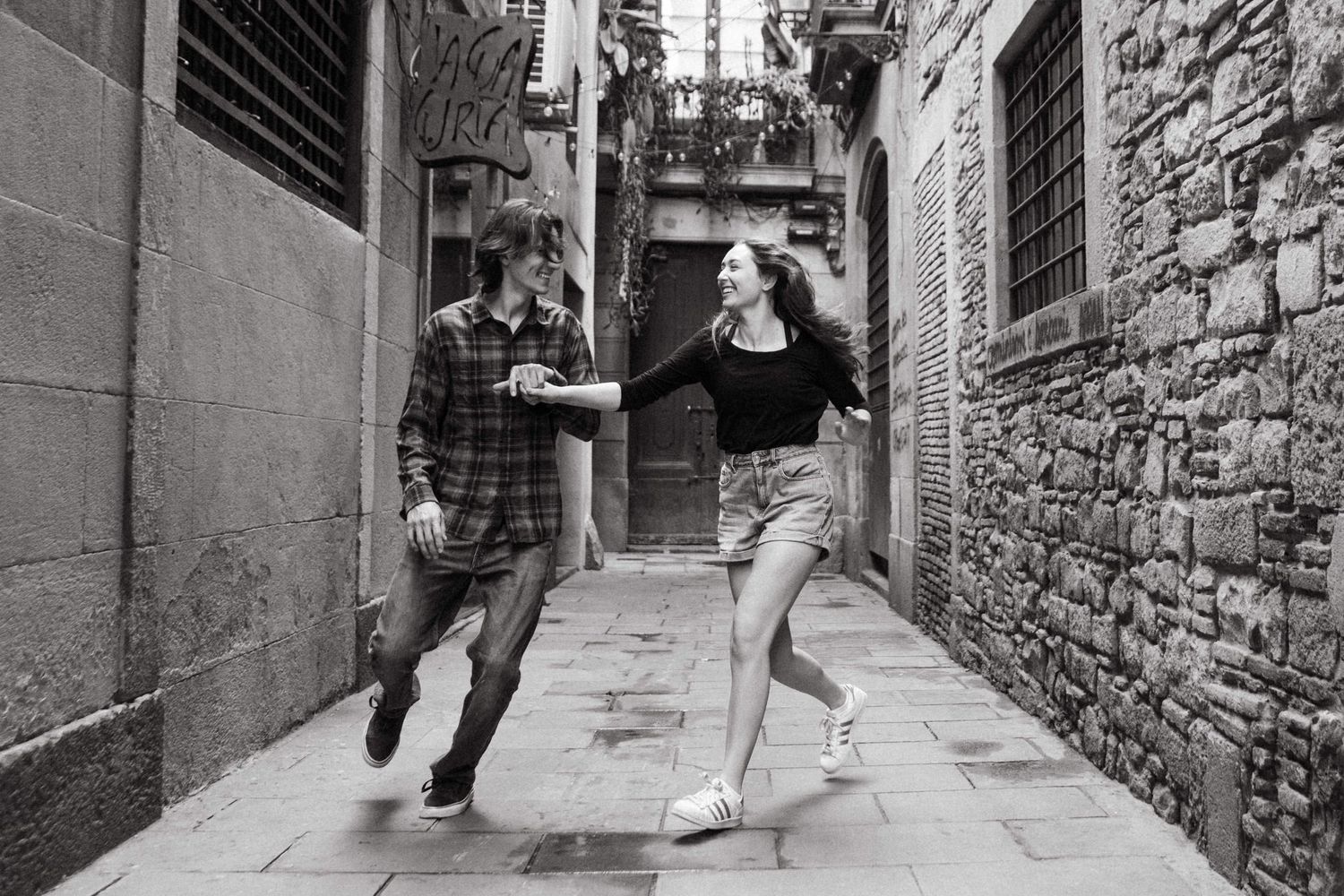 A couple walks playfully through narrow stone alleyways in an old European city.