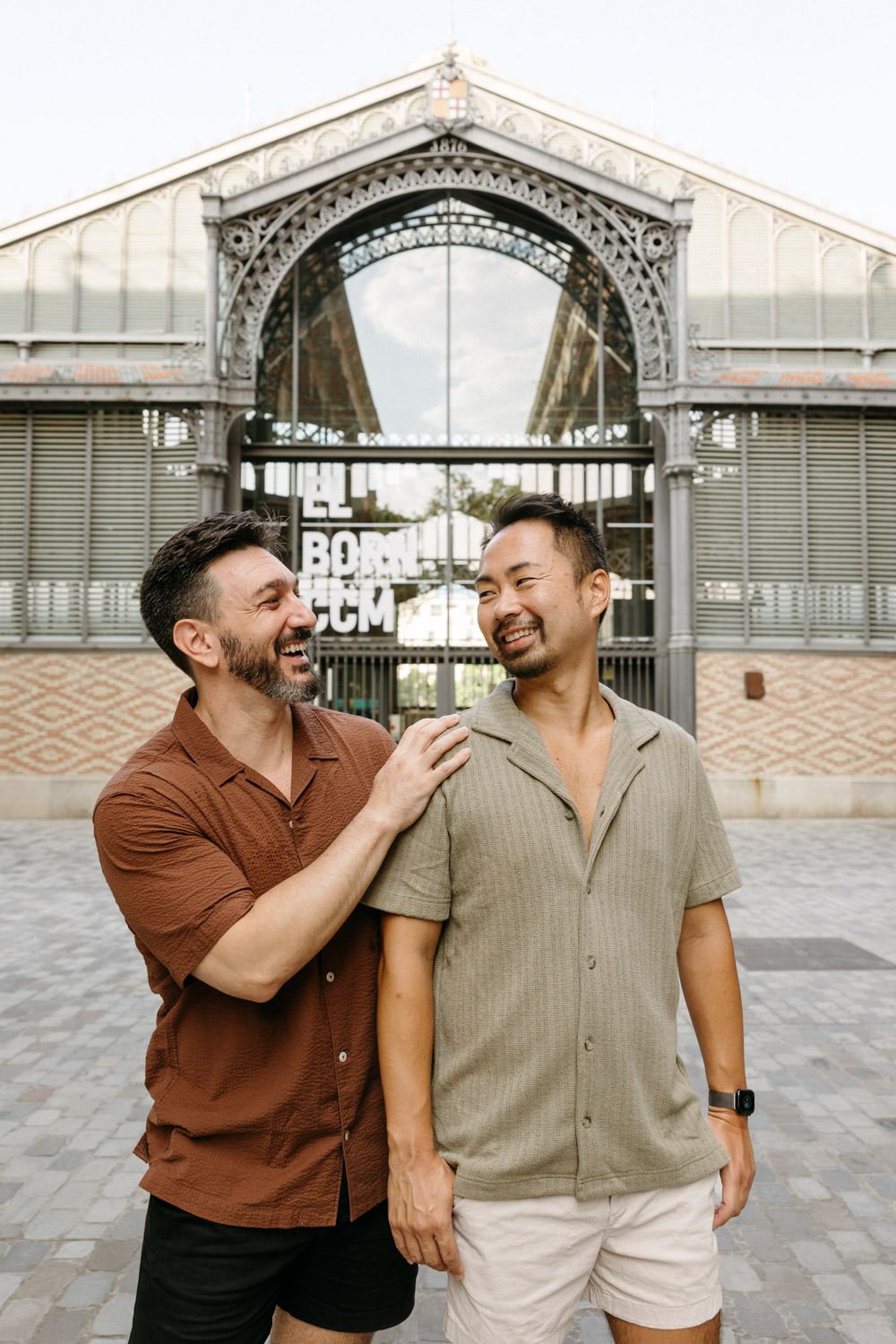 Two friends sharing a candid moment and laughing together in front of an ornate glass and iron archway.