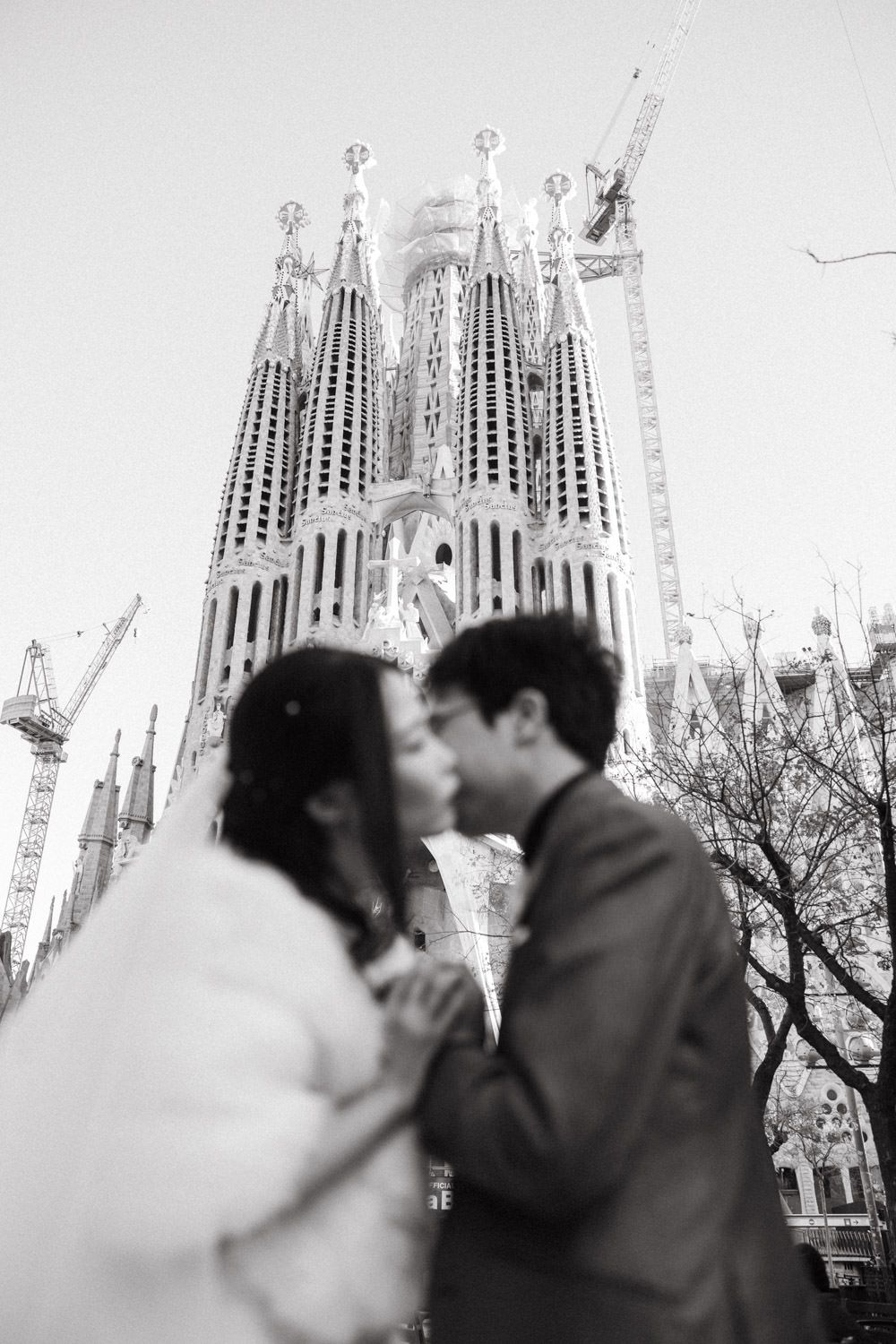Romantic couple sharing a kiss in front of the majestic Sagrada Familia cathedral spires in Barcelona.
