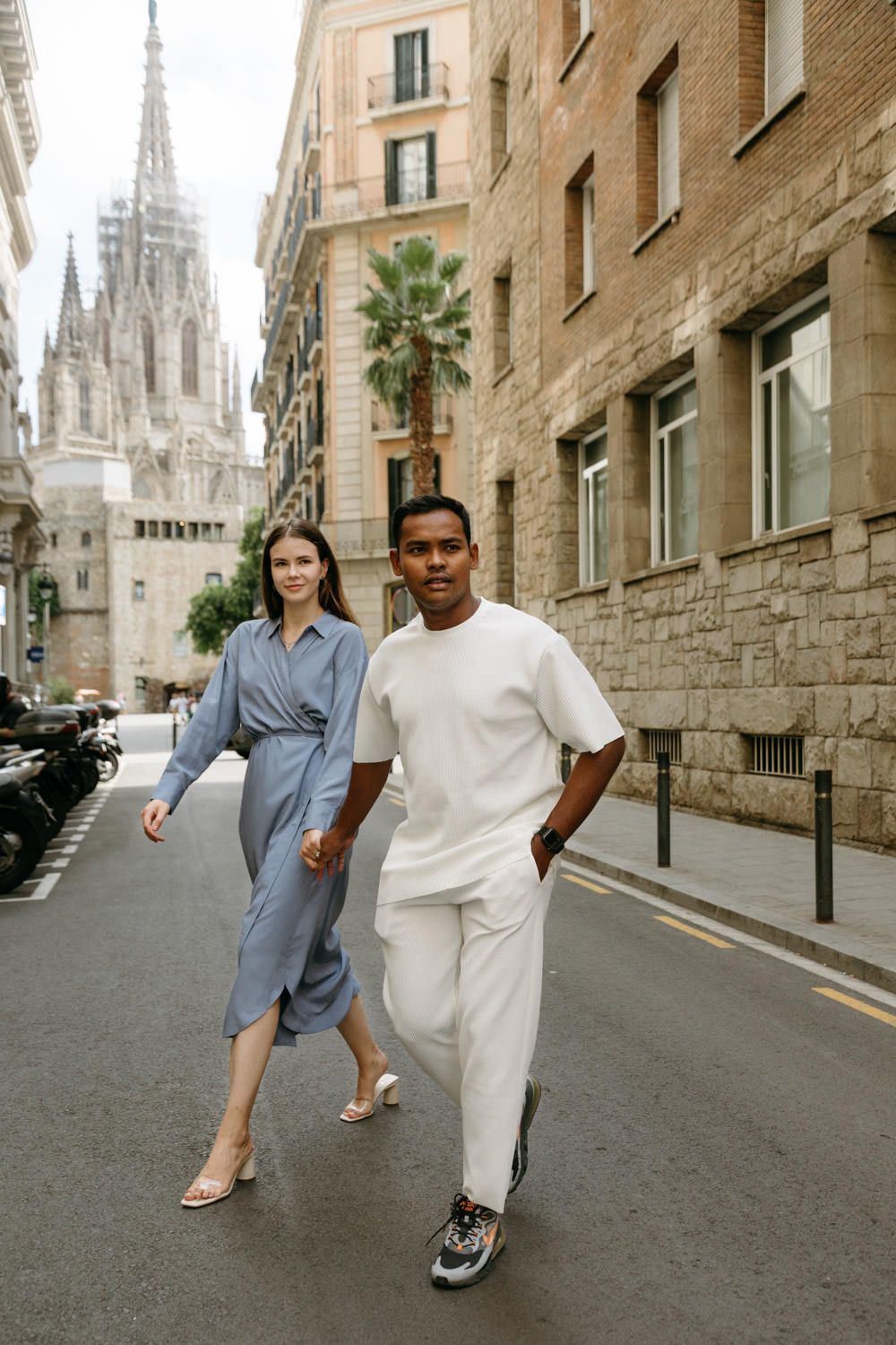 People walking and posing playfully on a historic cobblestone street with a Gothic cathedral in the background.