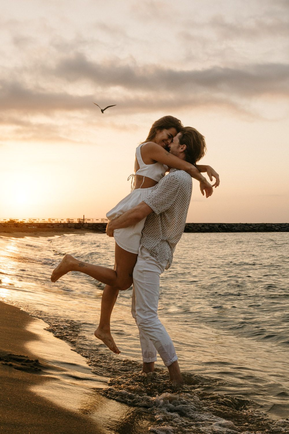 Couple in white embracing during sunset on a romantic beach photoshoot.