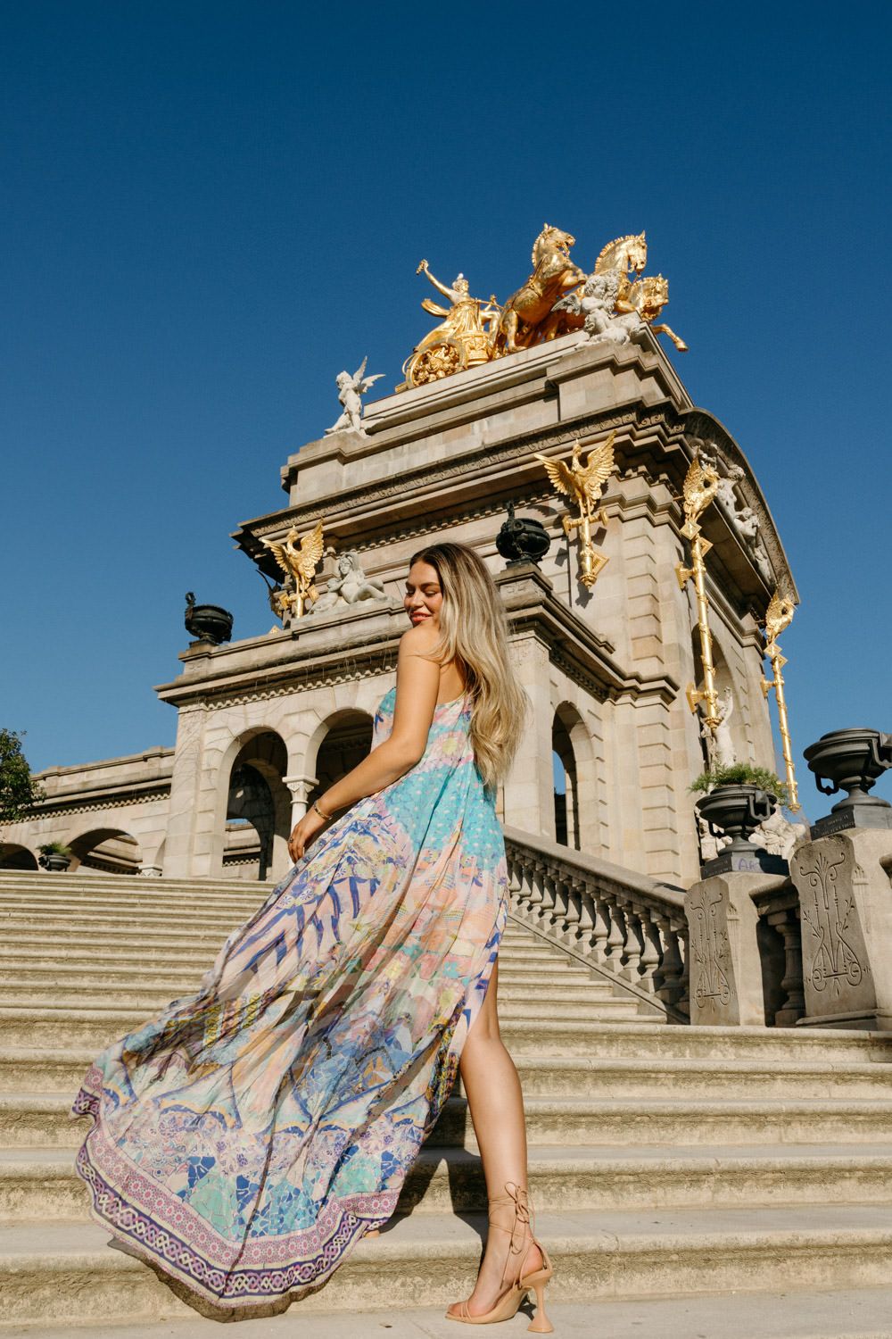 A flowing summer dress photographed on ornate stone steps against a bright blue sky.