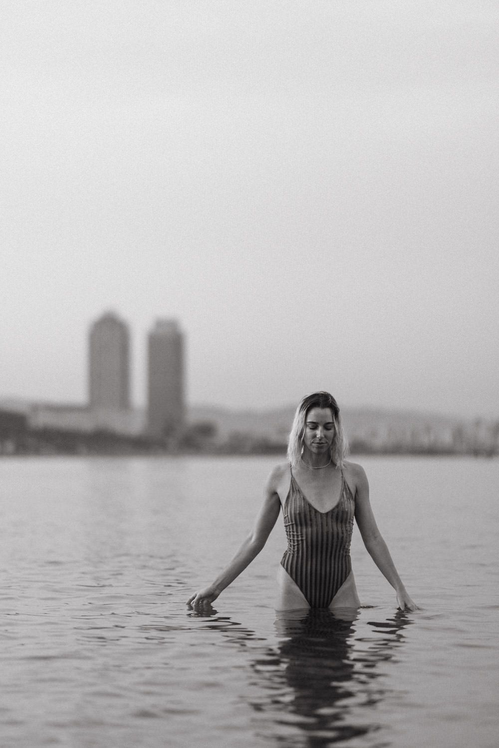 Artistic black and white photo of a swimmer in a striped suit wading in calm waters.
