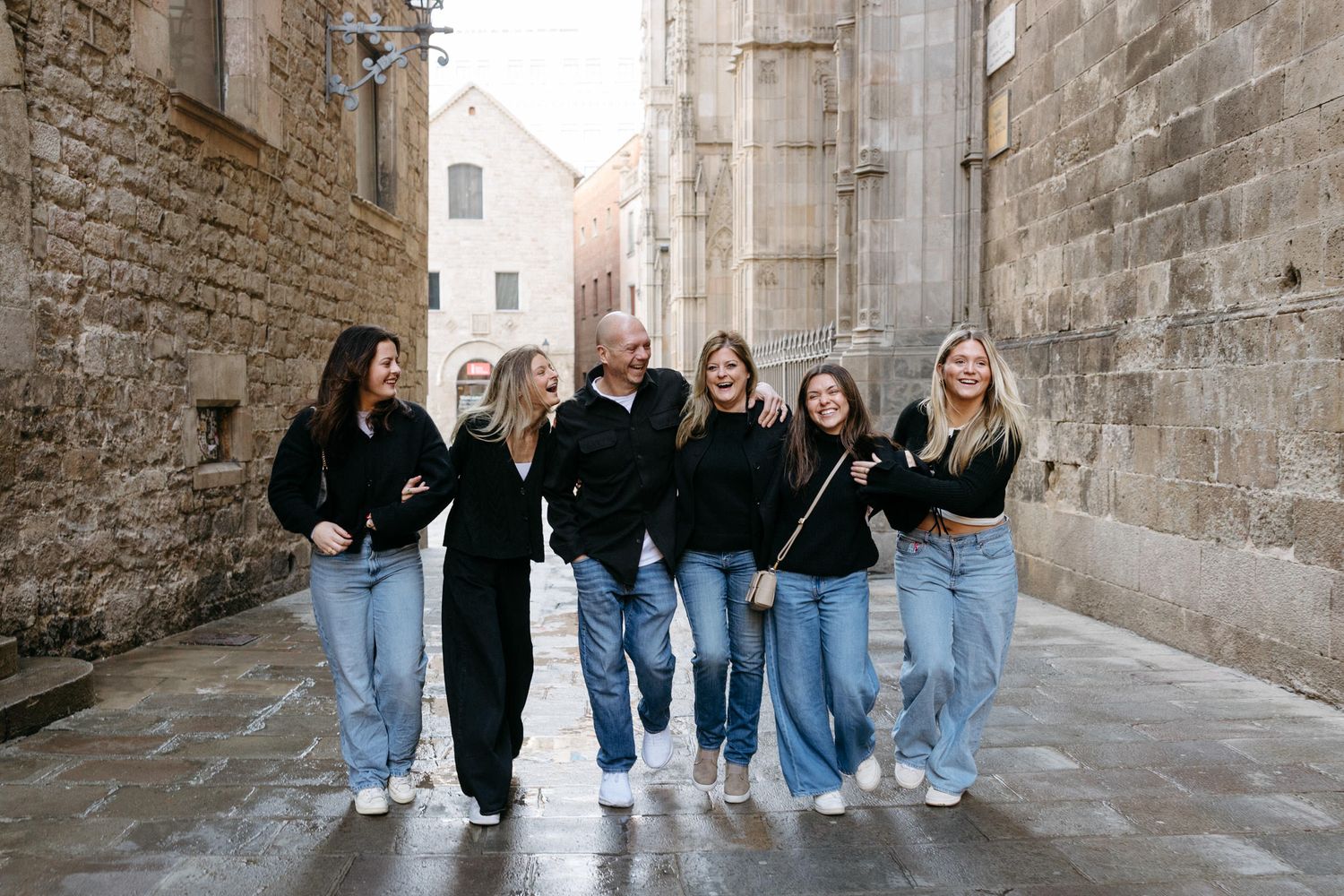 Group photo of friends in matching denim and dark outfits posing against a stone wall in Barcelona.