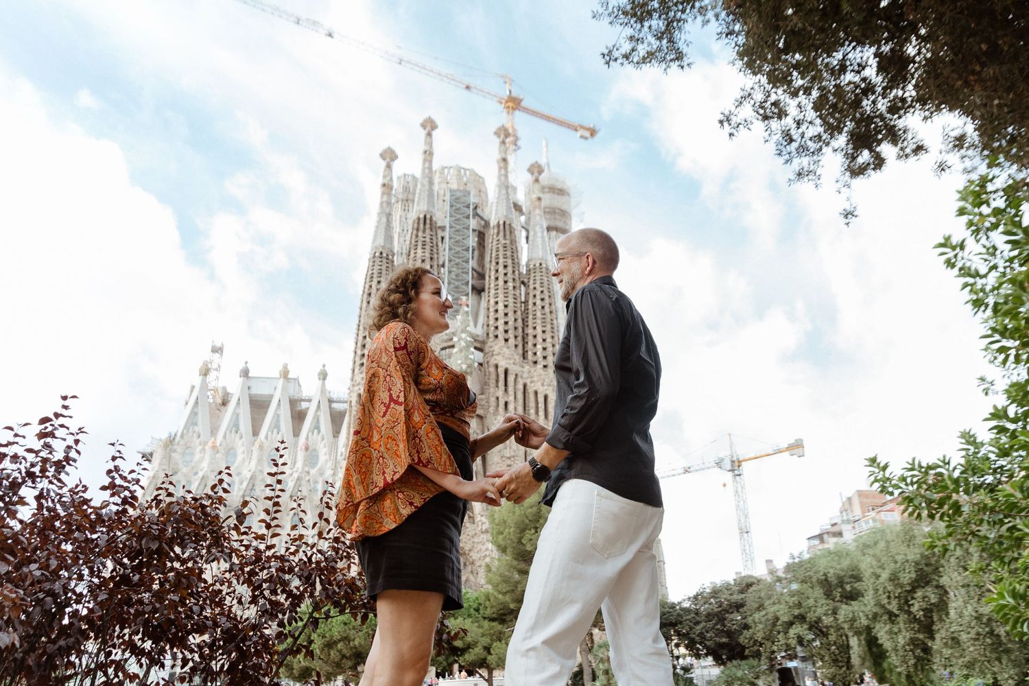 A couple shares a romantic moment with La Sagrada Familia cathedral visible in the background.