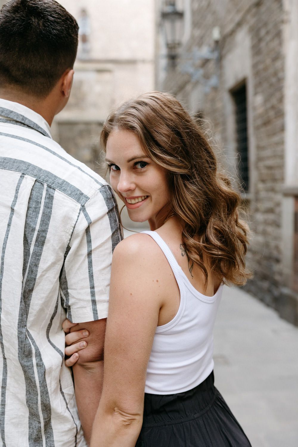 Couple poses playfully in a narrow European alleyway wearing casual summer outfits.