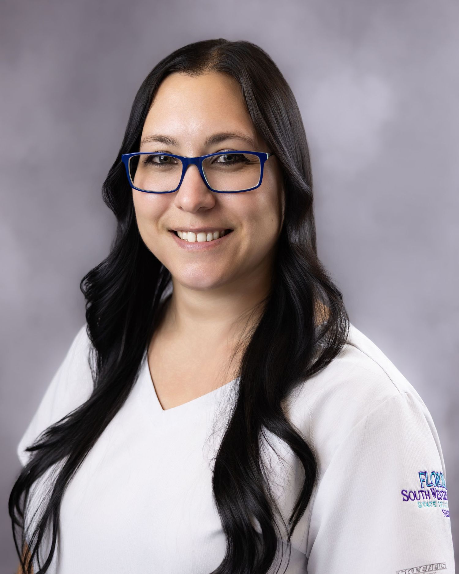 Smiling woman with long dark hair and blue glasses wearing a white Florida SouthWestern State College uniform shirt.