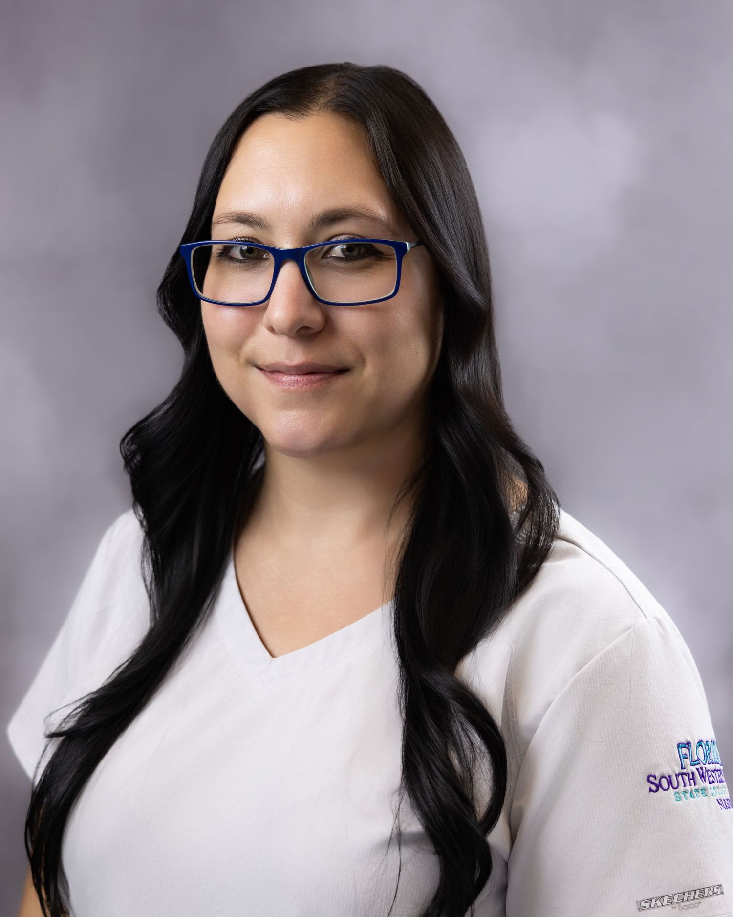 A young woman with long dark hair and blue glasses wearing a white medical uniform with a Southwest university logo.