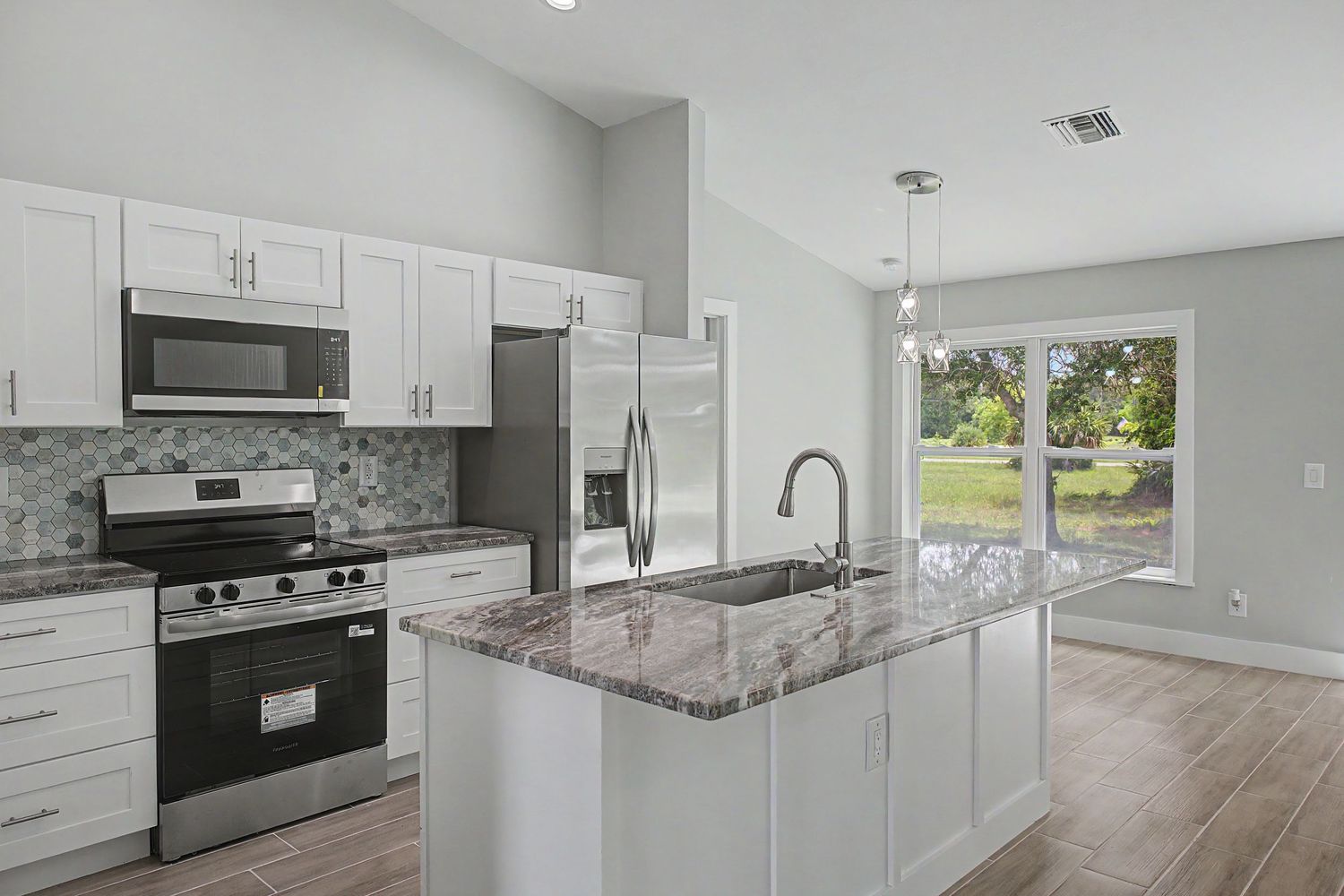 Bright modern kitchen with white cabinets, granite island with sink, stainless steel appliances, mosaic backsplash and wood-look flooring.