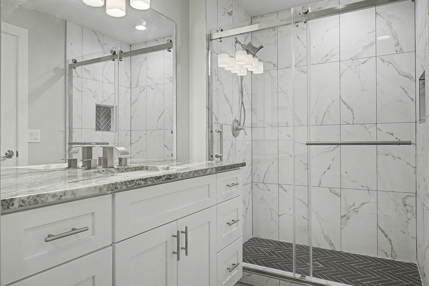 Modern bathroom with white shaker vanity, granite countertop, and a glass-enclosed walk-in shower with marble-look tile and mosaic floor.