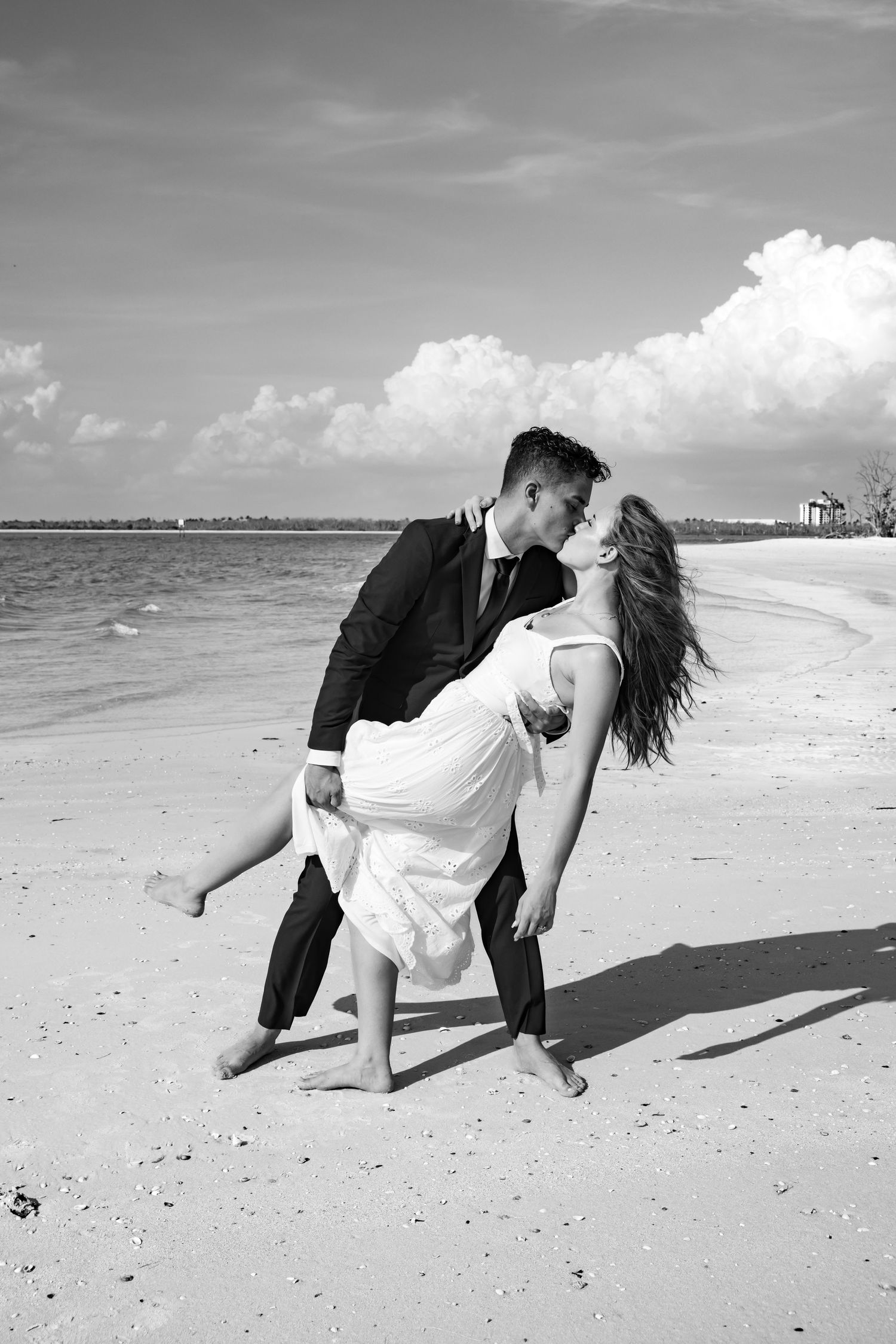 Black and white photo of groom dipping bride for a kiss on a sandy beach.
