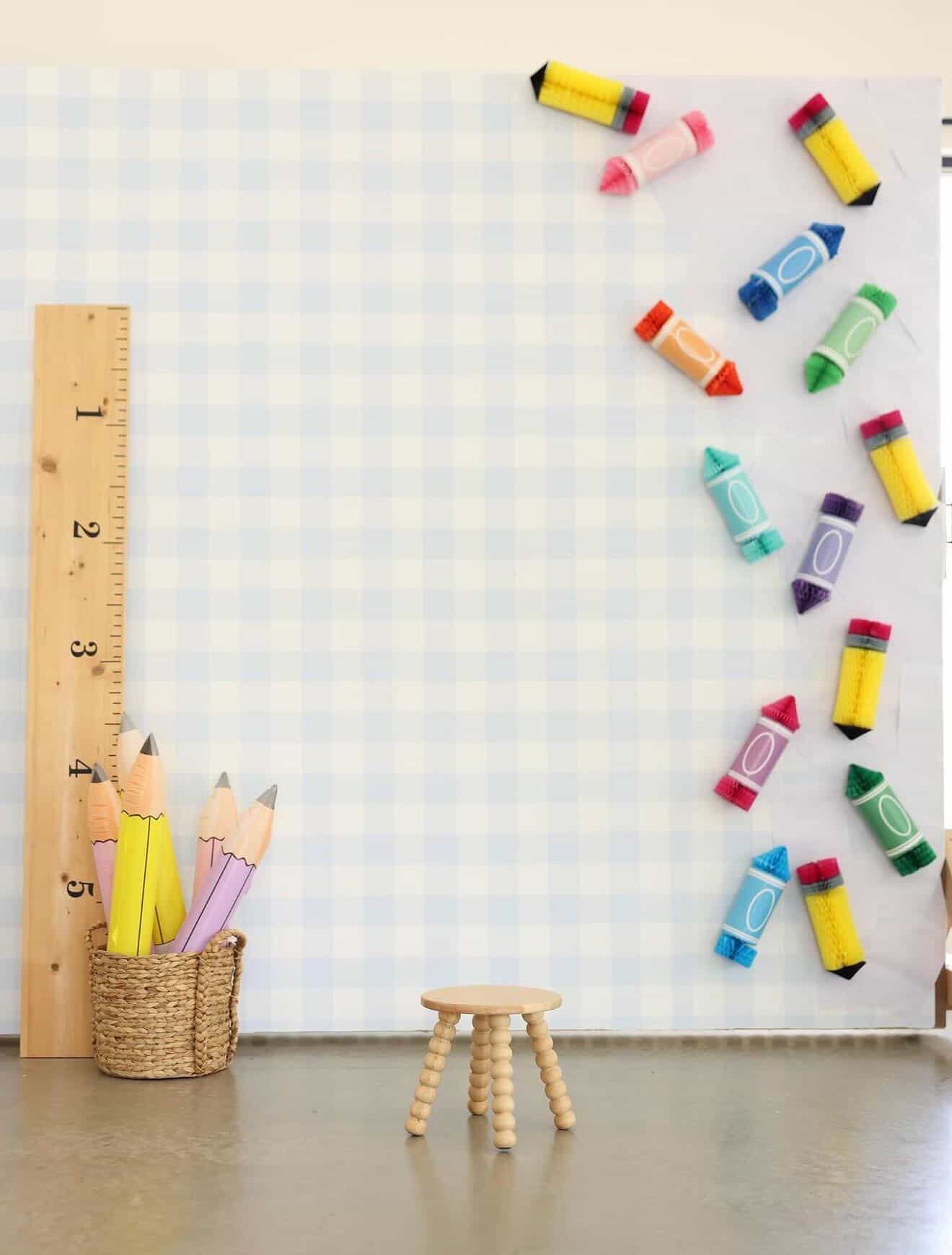 Playful back to school backdrop with gingham pattern, giant ruler, pencils, and crayons.