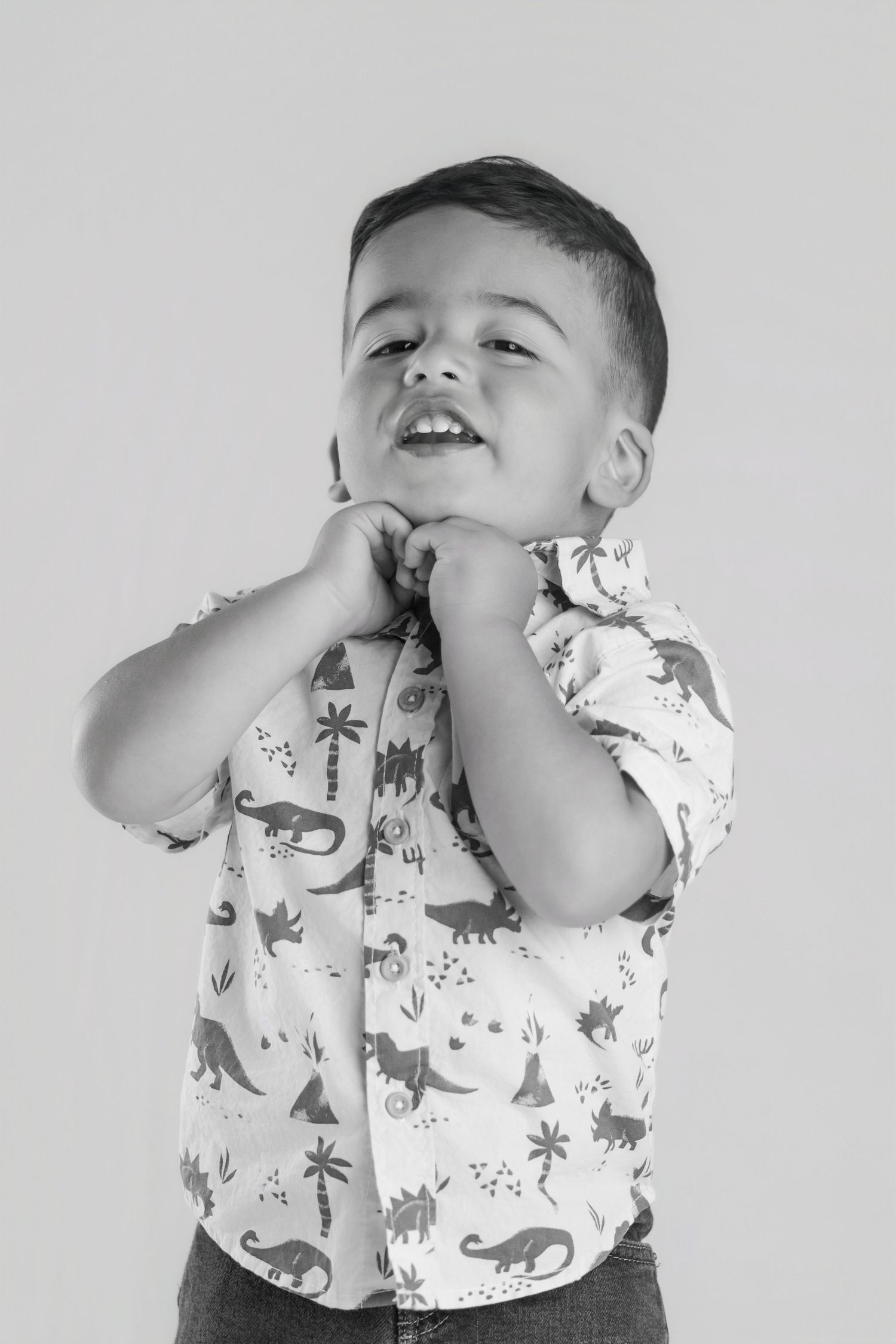 Black and white portrait of a smiling toddler boy in a dinosaur print button-up shirt.
