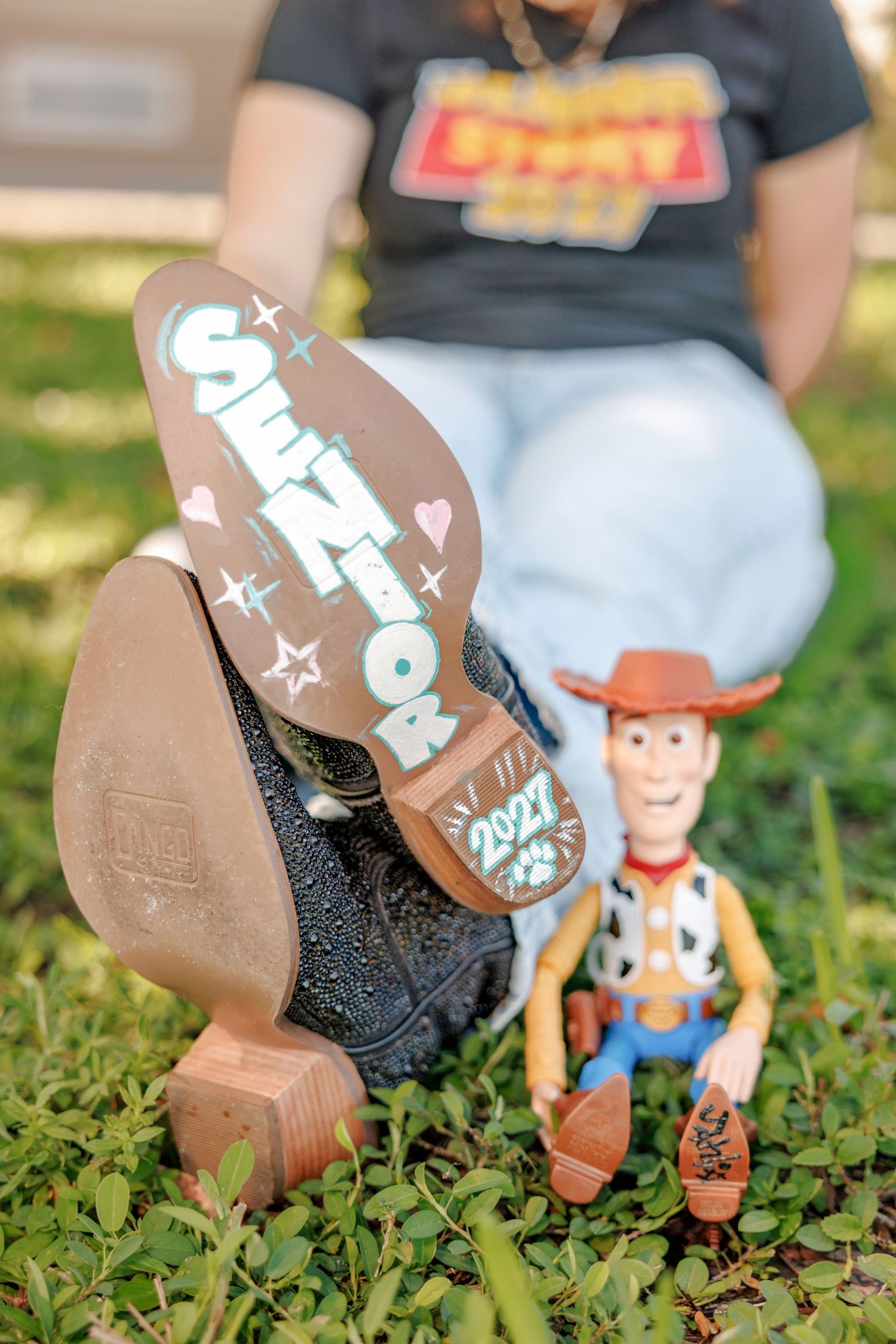 Senior 2021 painted on a cowboy boot sole beside a Woody toy figure in the grass, a creative class of 2021 graduation photo idea.