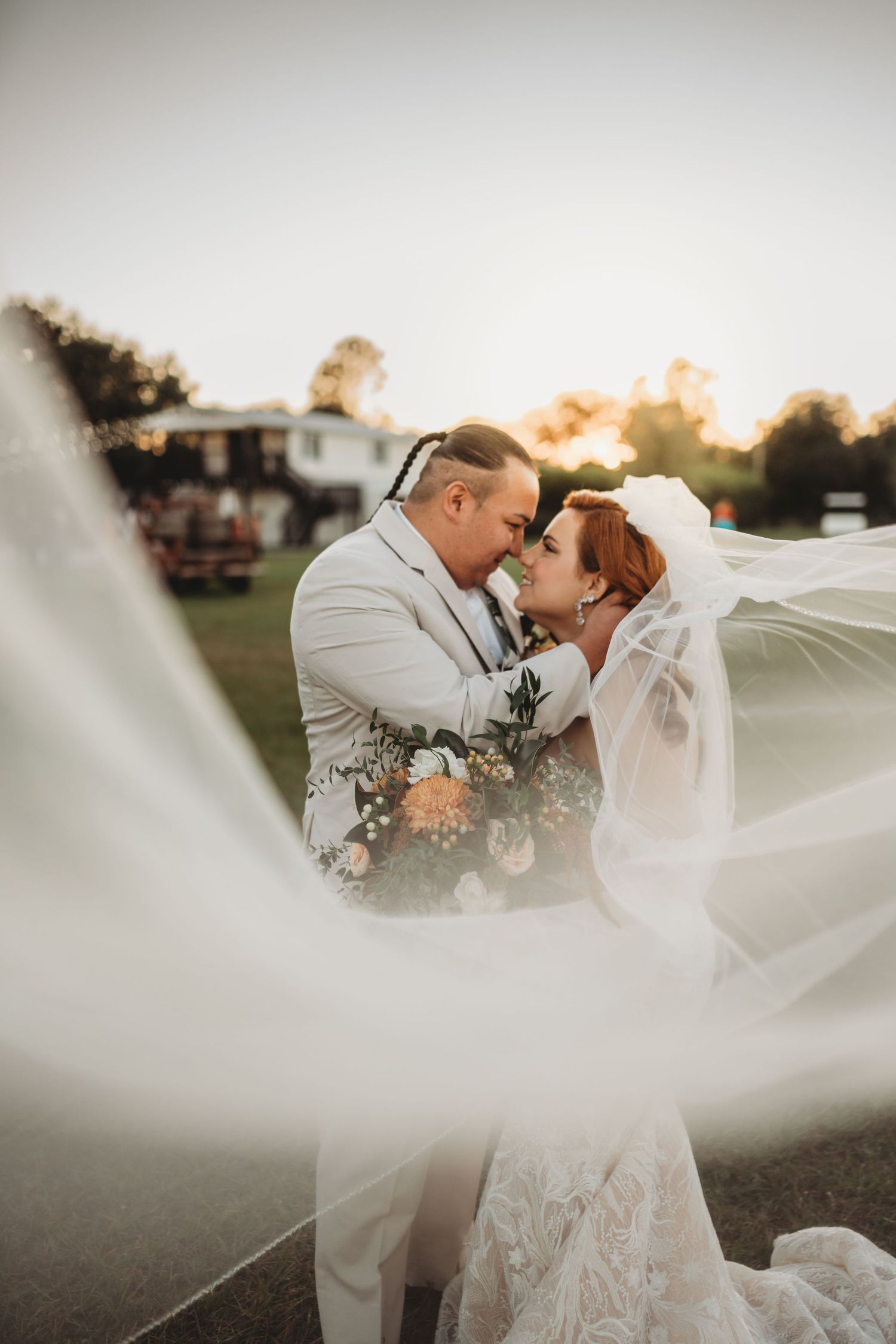 Wedding couple embracing during sunset with the bride's veil flowing beautifully in the golden light.