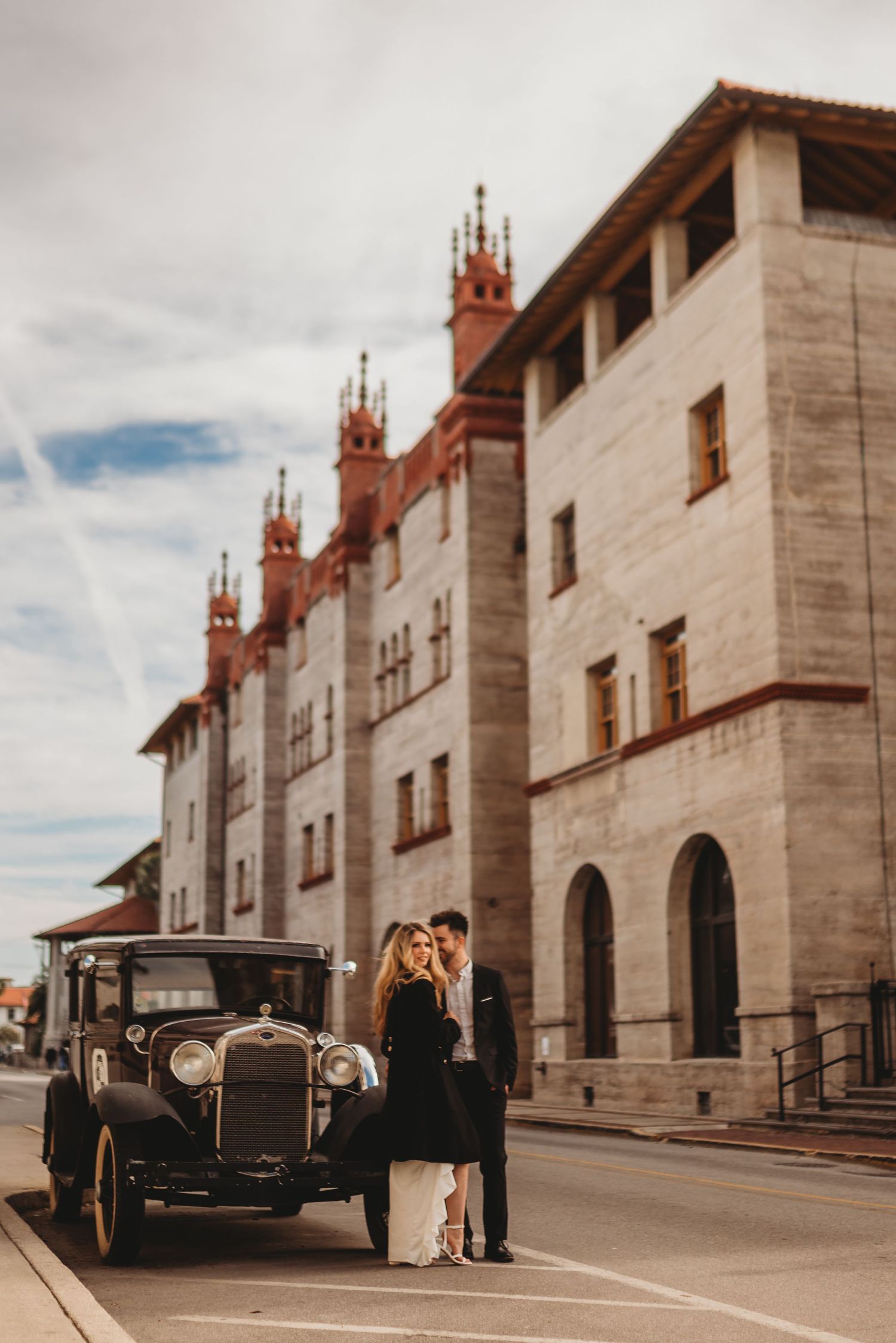 A vintage black car parked in front of an elegant historic building with stone architecture and decorative spires.
