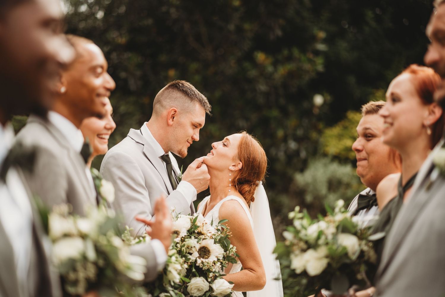 Joyful wedding party laughing together outdoors with bride and groom in center.