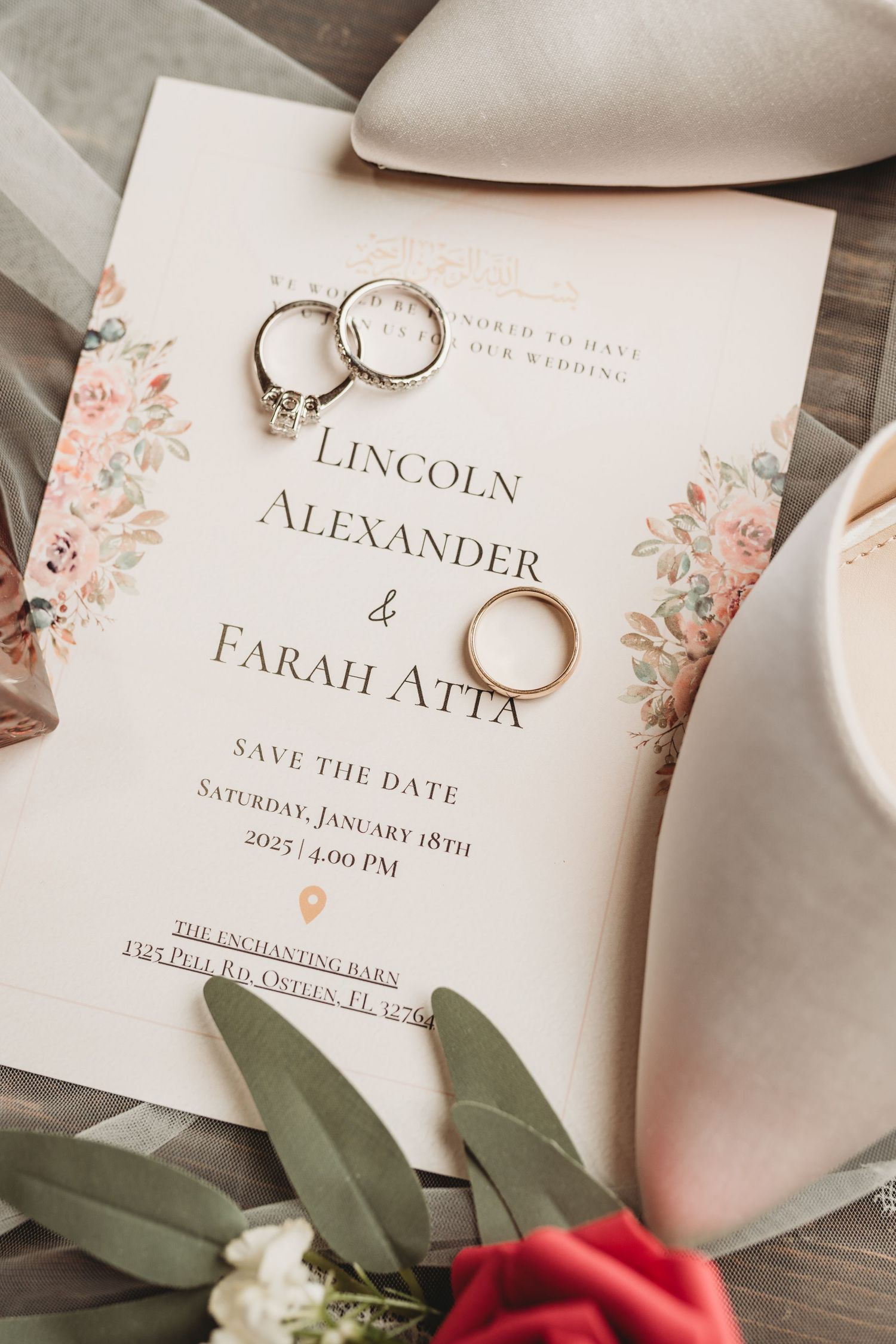 Elegant wedding save-the-date invitation with gold rings and floral designs laid on wood with rose petals.