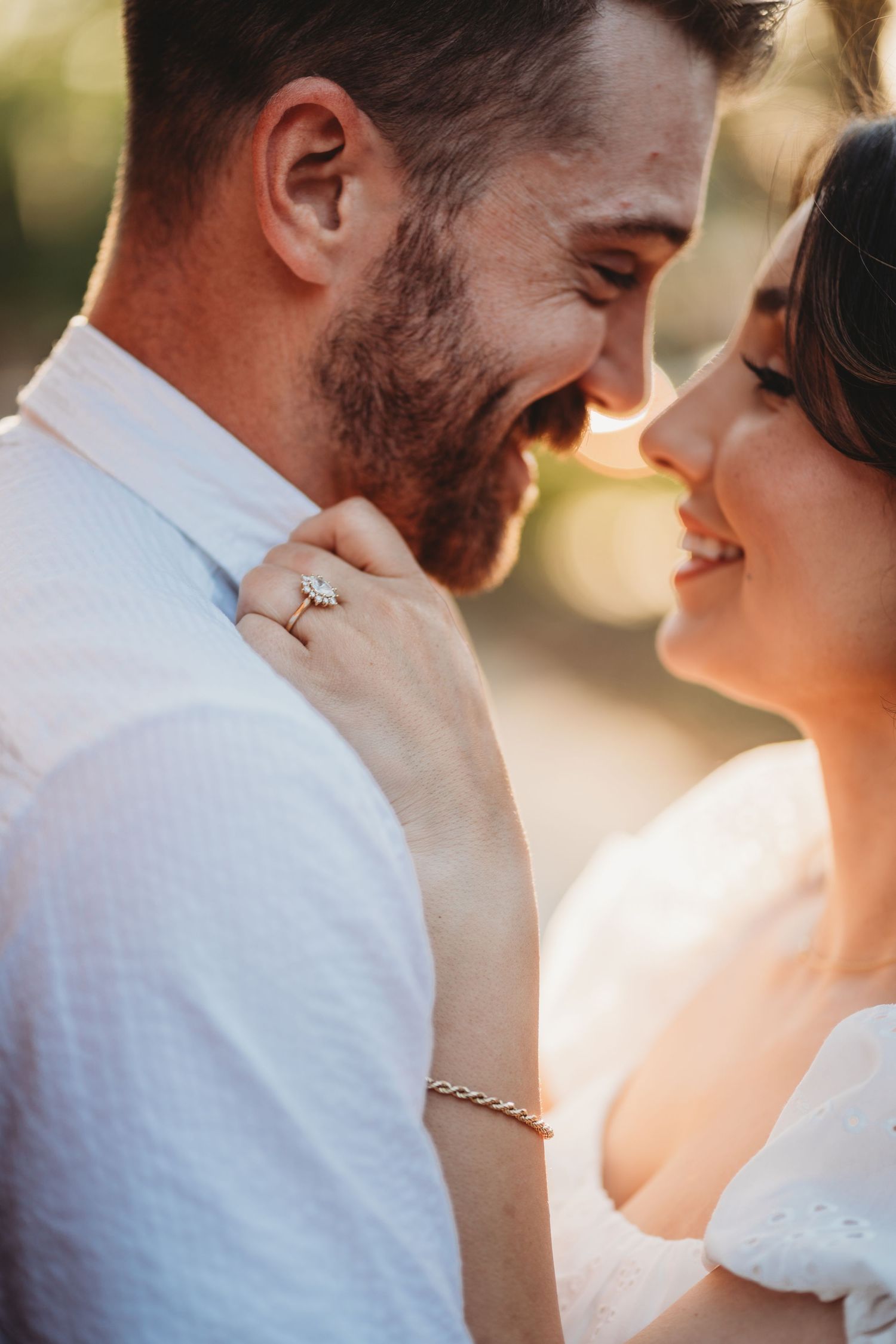 Happy couple shares an intimate moment together in sunlit wedding portrait showing loving smiles and ring details.
