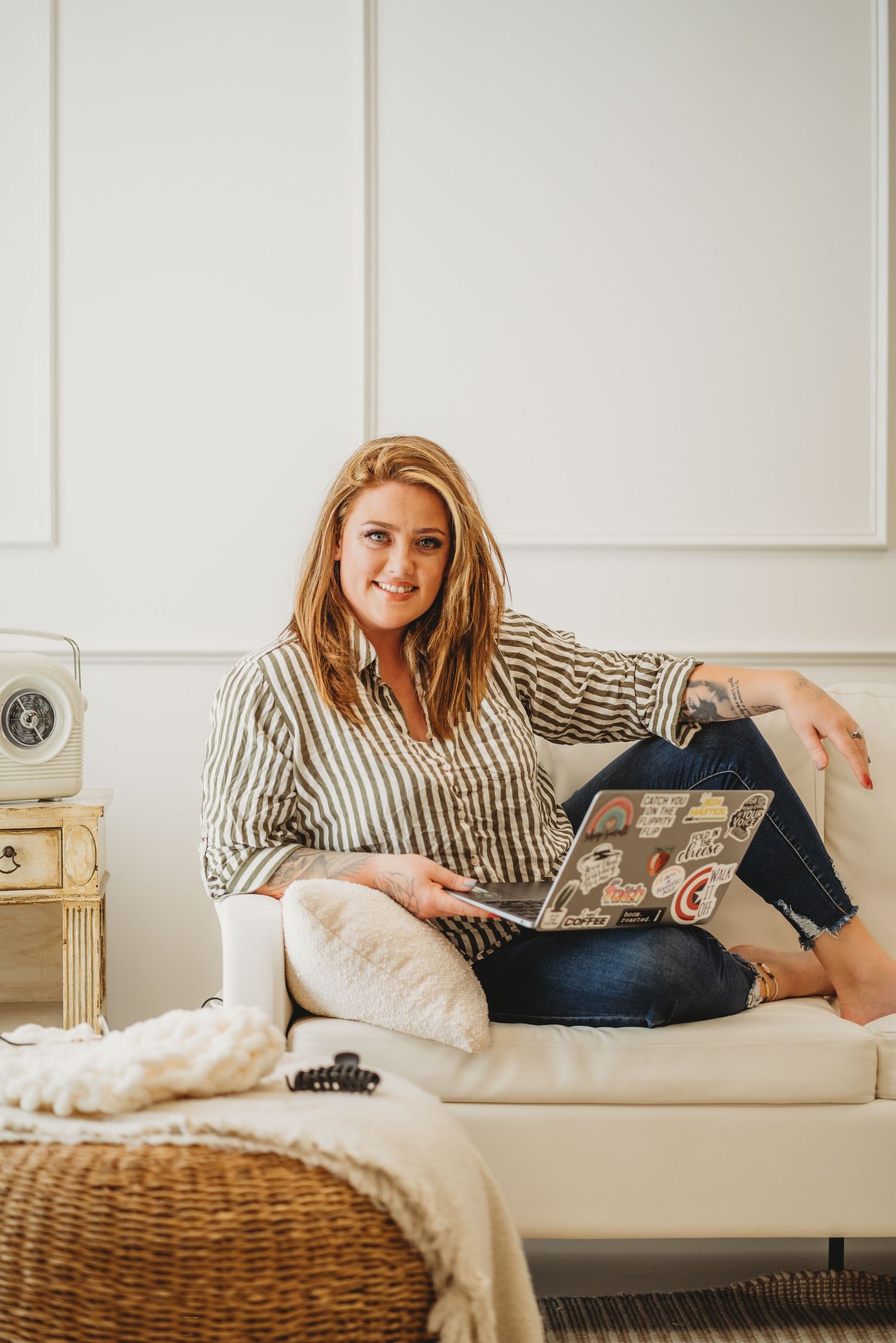 Person relaxing on white couch with striped shirt while reading magazine in cozy living room setting.