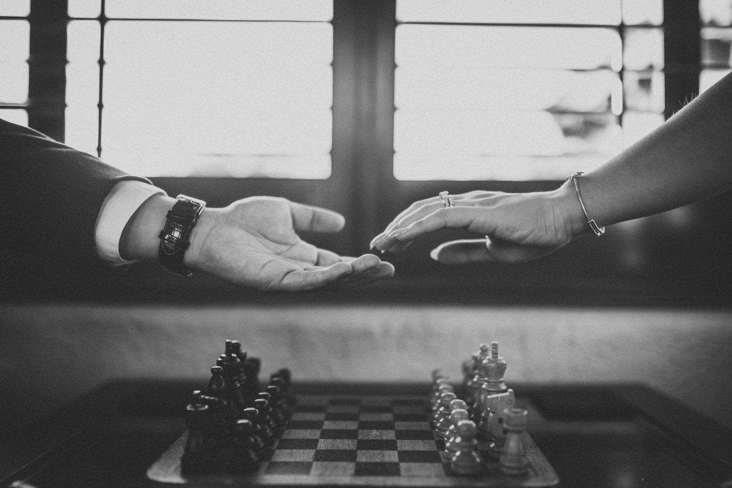 Hands reaching across chess board in black and white dramatic lighting.