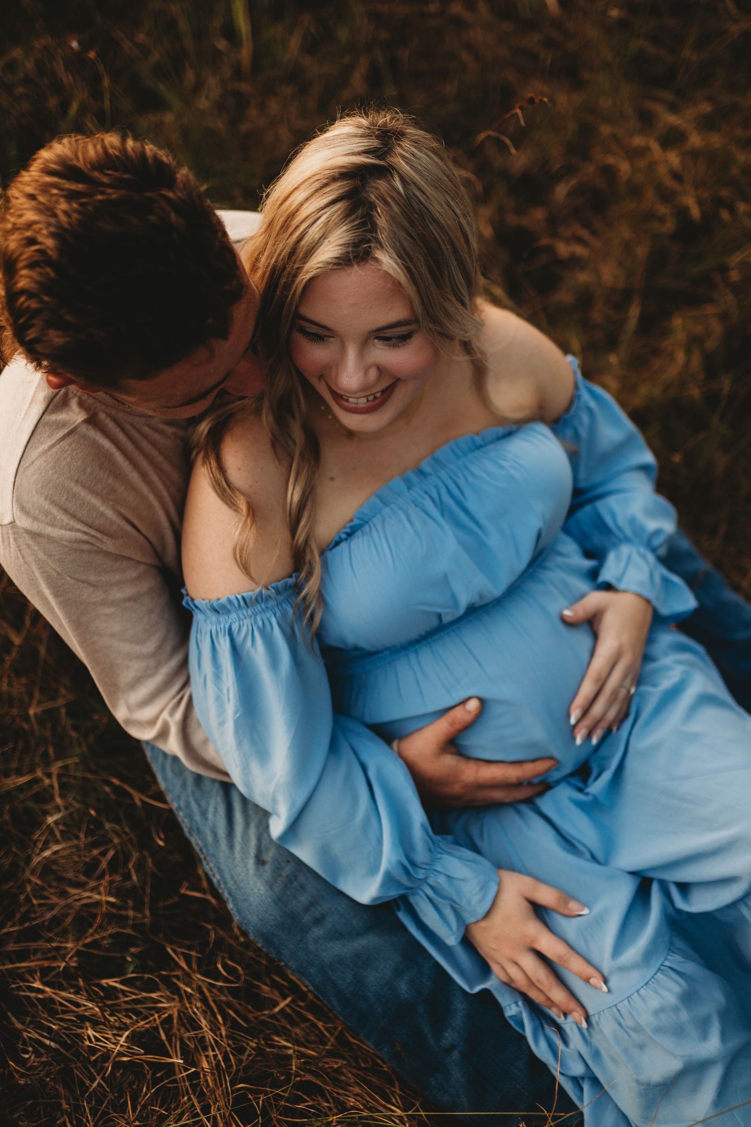 A loving couple shares an intimate moment outdoors as they anticipate their new arrival in a flowing blue maternity dress.