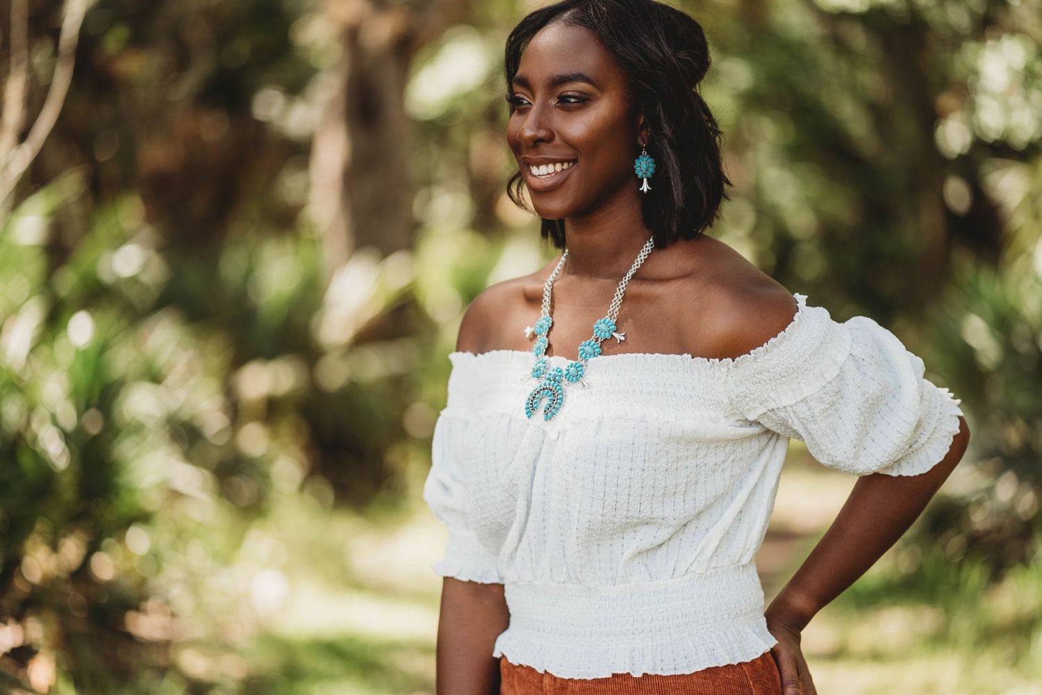 Beautiful off-shoulder white blouse paired with turquoise statement necklace against lush outdoor garden backdrop.