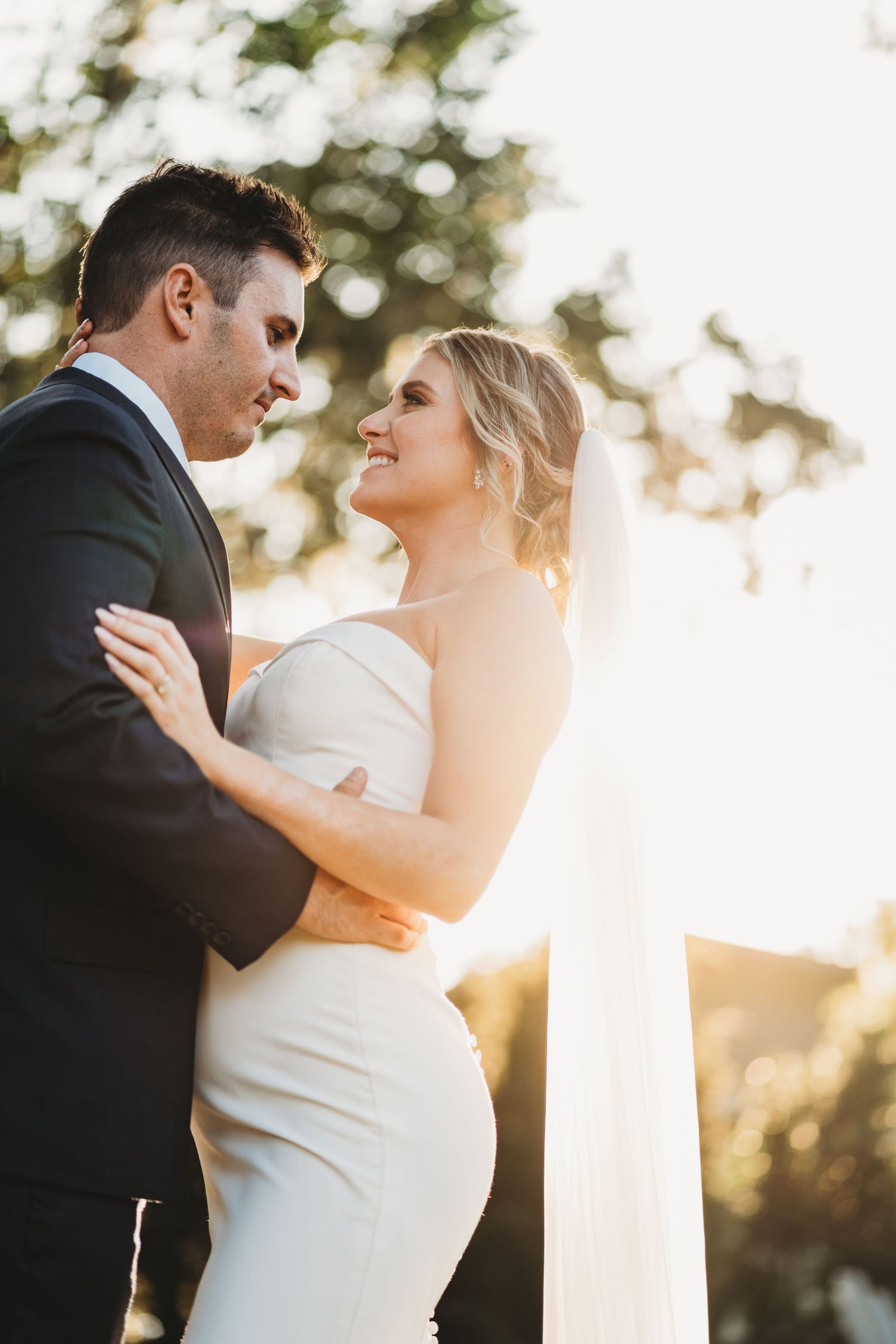Romantic wedding portrait of newlyweds embracing during golden hour sunset outdoors.