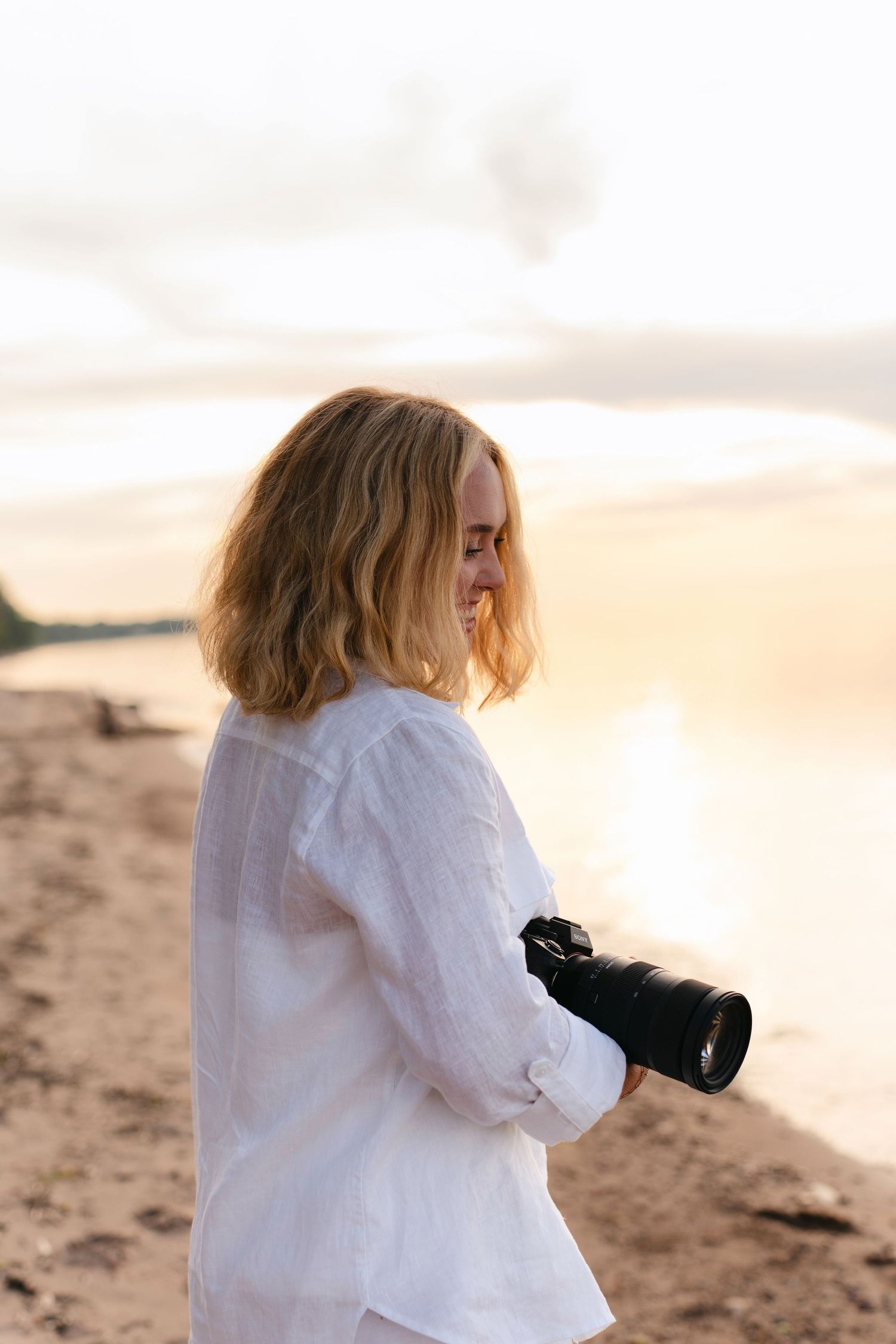 Person in white shirt sits on sandy beach during golden sunset hour.