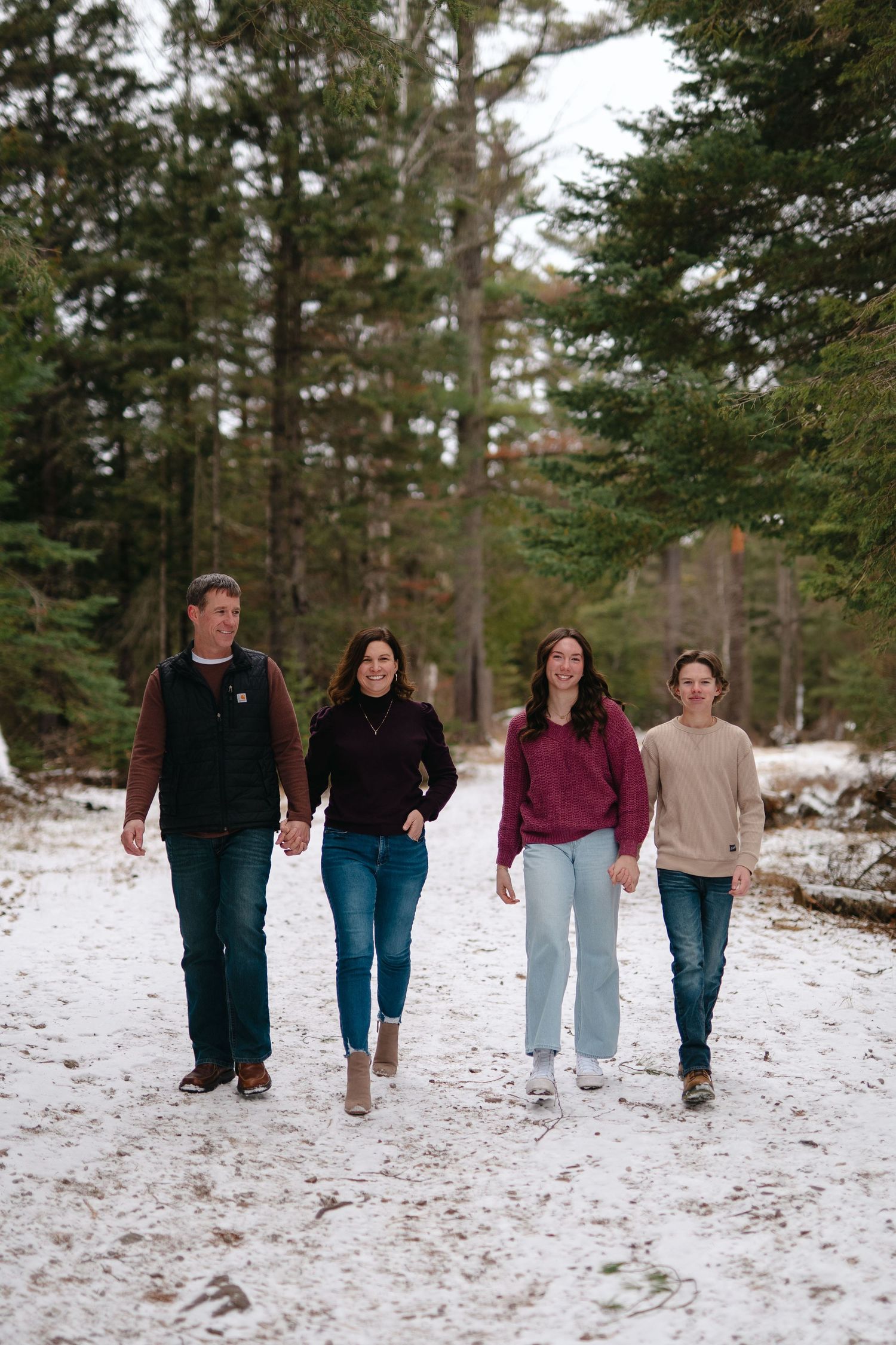 A group of people walking together in a snowy forest setting wearing casual winter clothing.