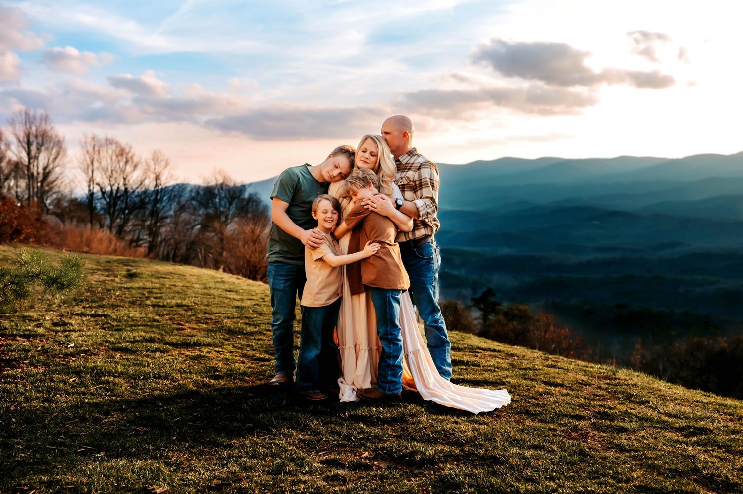 A couple embraces on a hilltop overlooking a scenic mountain landscape at sunset.