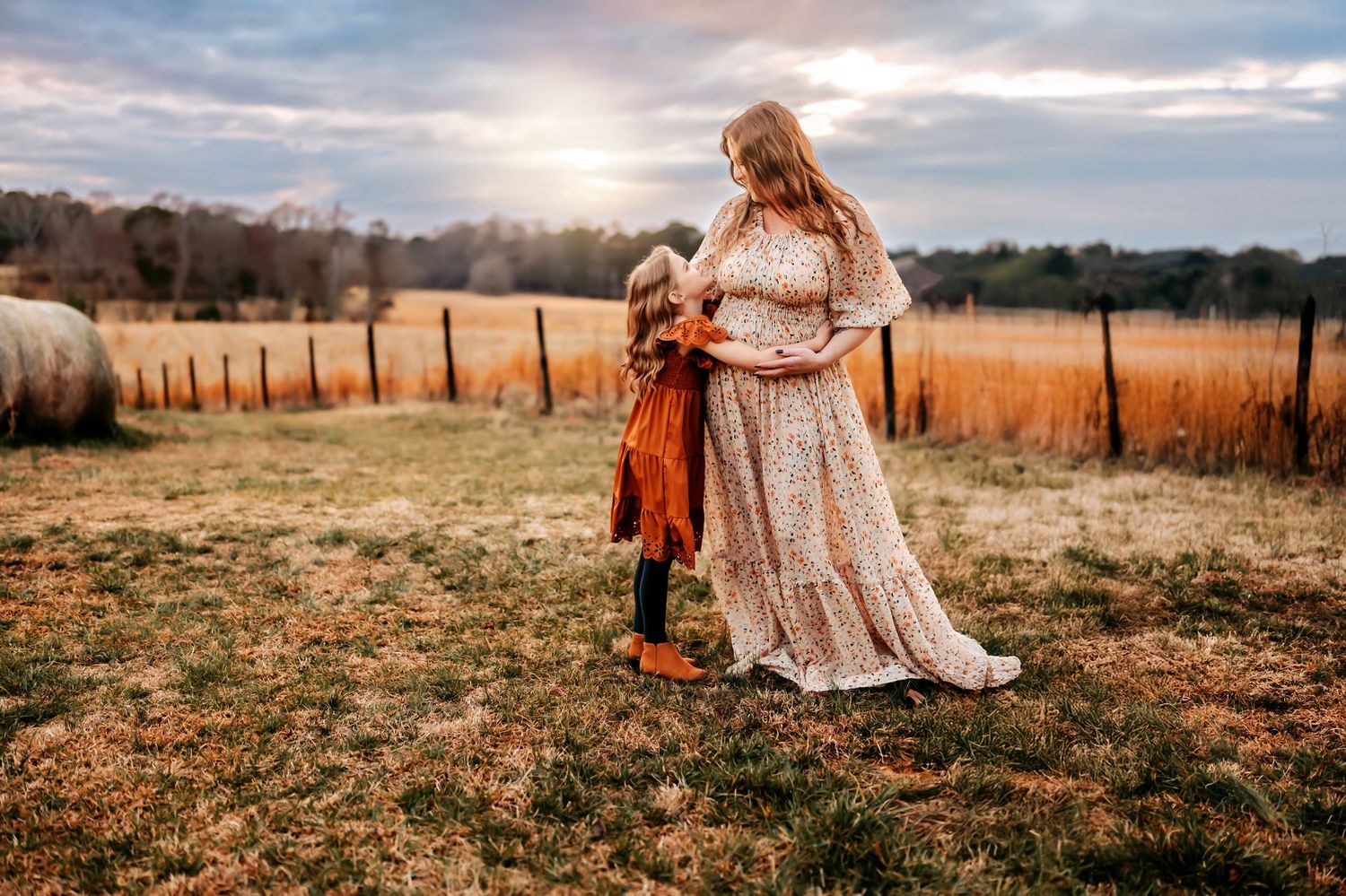 A warm sunset illuminates a rustic field scene with figures in a flowing dress and autumn-colored clothing at golden hour.
