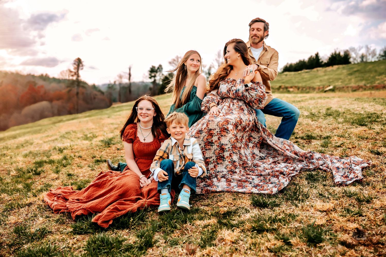 A group enjoys a cozy autumn picnic on a grassy hillside with colorful blankets spread out on the ground.