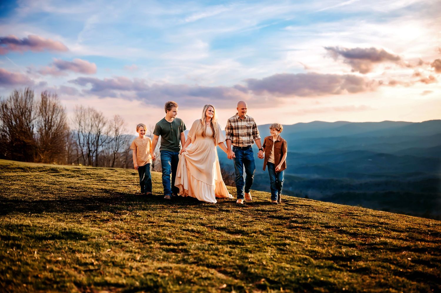 A group of people stand silhouetted on a hilltop against a dramatic sunset sky with mountain vistas in the distance.
