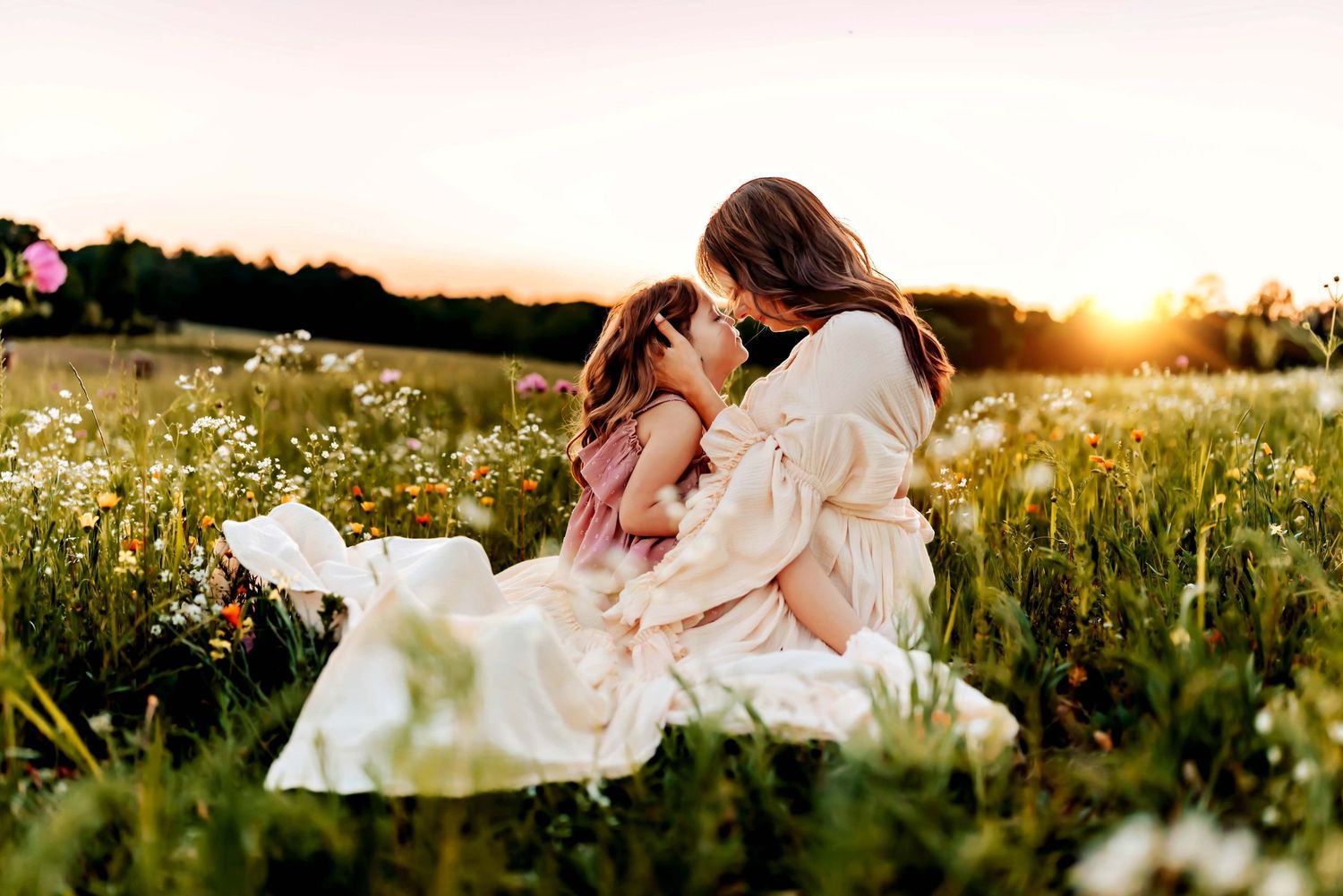 A tender moment between parent and child sitting in a wildflower meadow at golden hour sunset.